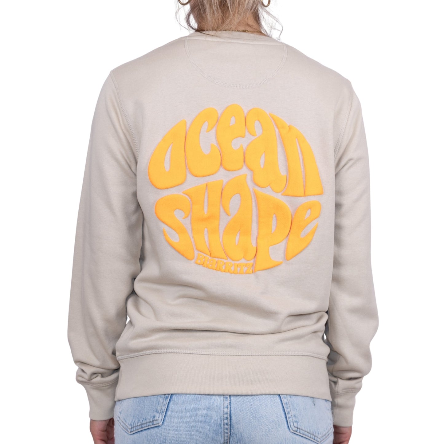 Sweat unisexe sans capuche Desert Dust avec grand logo bubble "ocean shape biarritz" orange fluo dans le dos, vu de dos sur mannequin femme