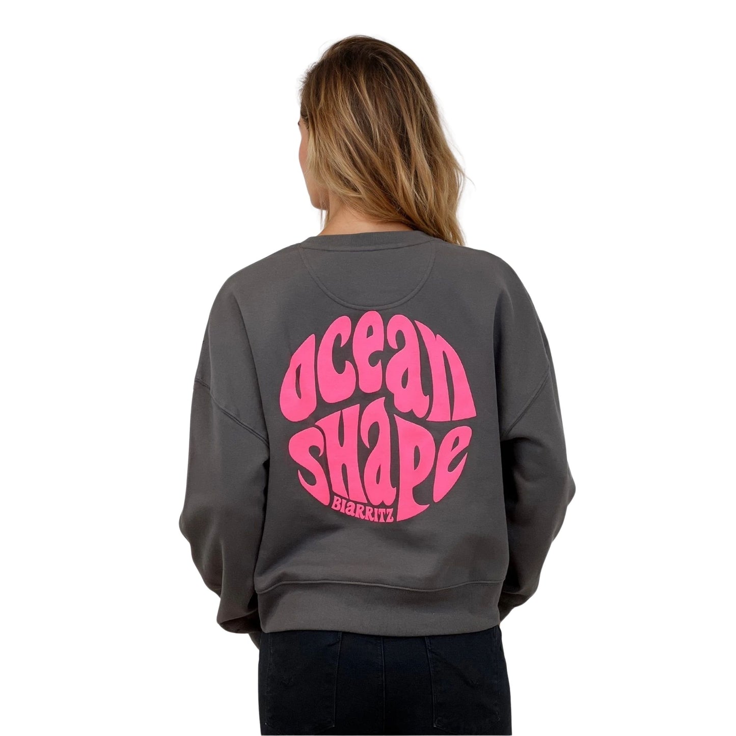 Sweat femme court et oversize, col rond, épaules tombantes, 100 % coton biologique, couleur gris anthracite.
Gros logo bubble "Ocean shape Biarritz" rose fluo.
Vu de dos sur mannequin femme.