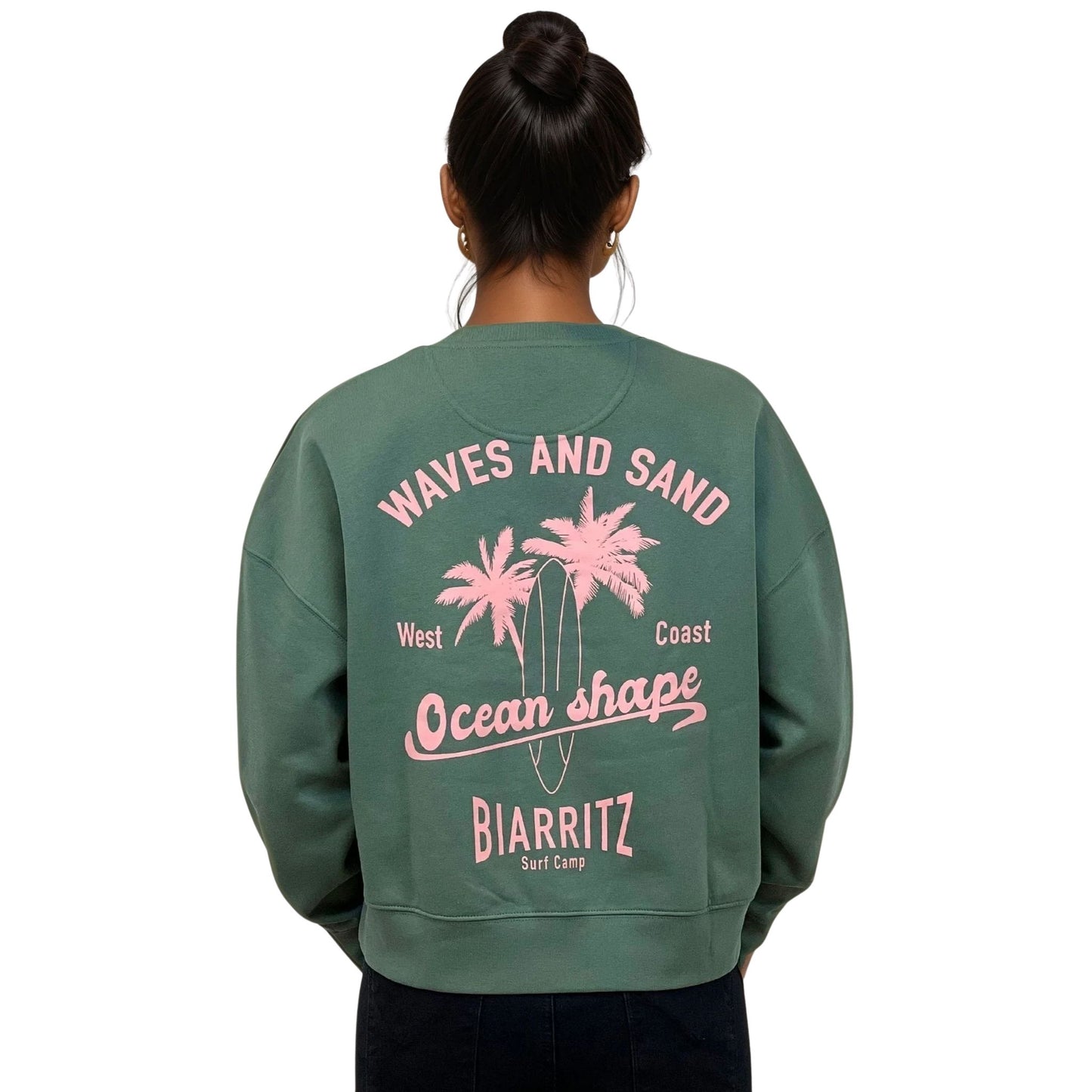 Sweat femme court et oversize, col rond, épaules tombantes, 100 % coton biologique, couleur vert sauge.
Grand dessin rose pâle de planche de surf et palmiers + écriture "Waves and sand, Ocean Shape Biarritz" dans le dos.
Vu de dos sur mannequin femme.