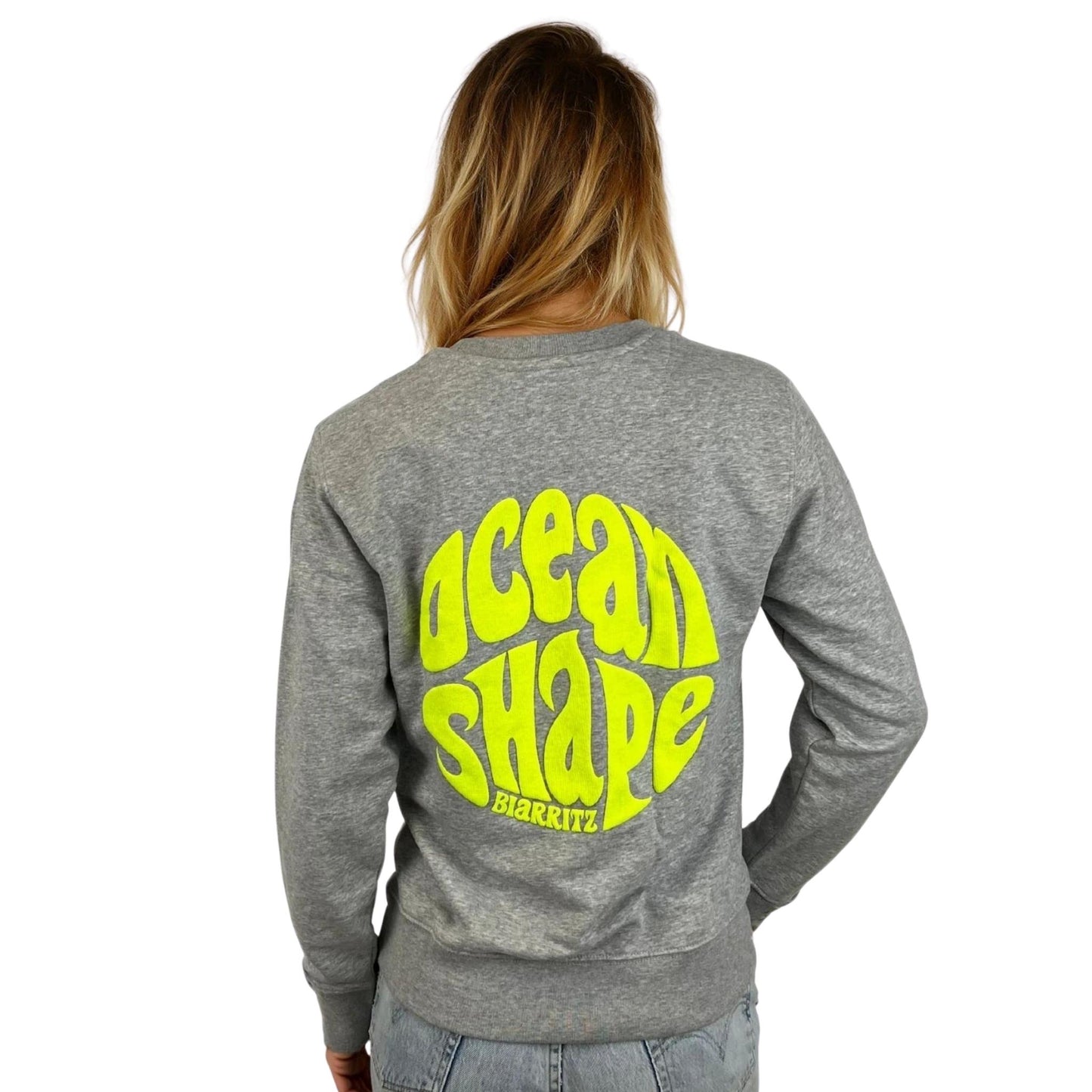 Sweat à col rond unisexe gris ocean shape, vu de dos sur mannequin femme.
Dos ; gros logo bubble "ocean shape biarritz" jaune fluo