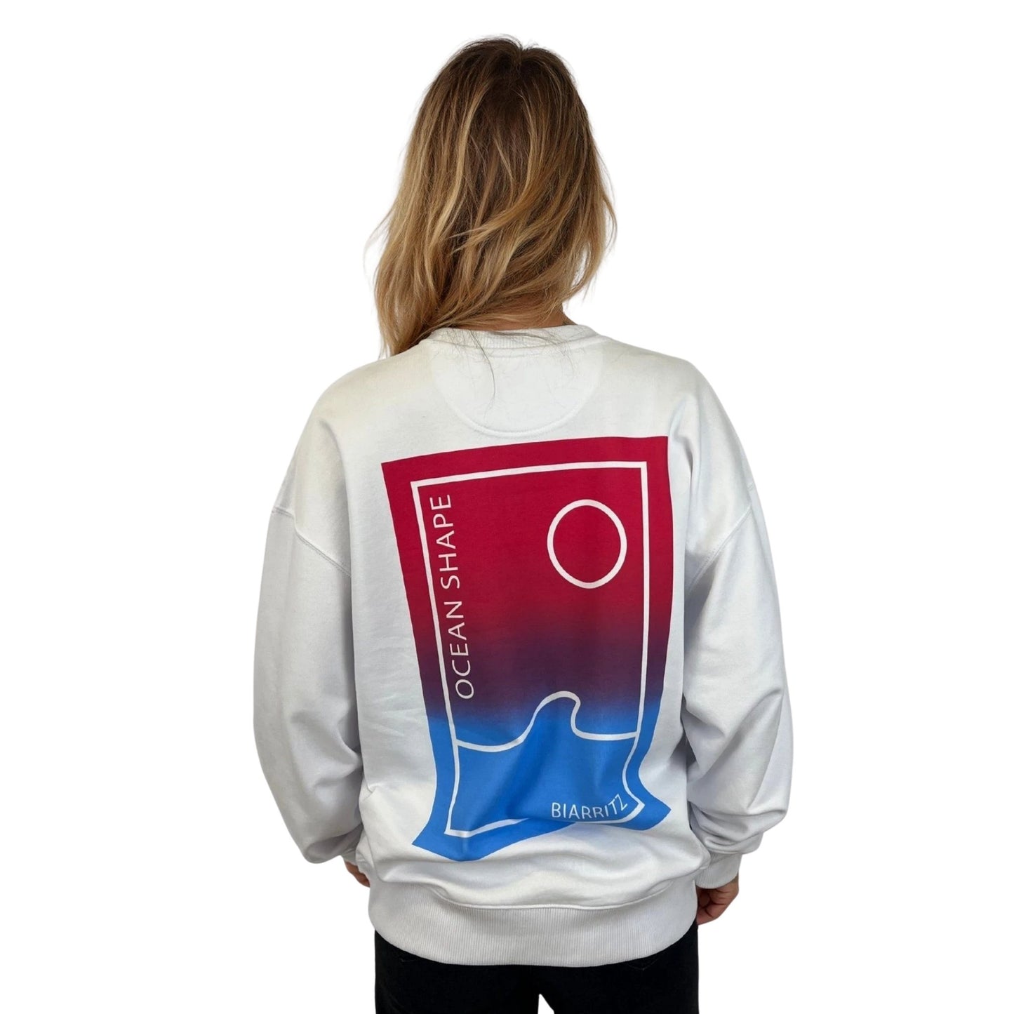 sweat à col rond unisexe Ocean Shape blanc, vu de dos sur mannequin femme.
Dos : même dessin en plus gros en dégradé rose et bleu avec écriture "ocean shape biarritz".