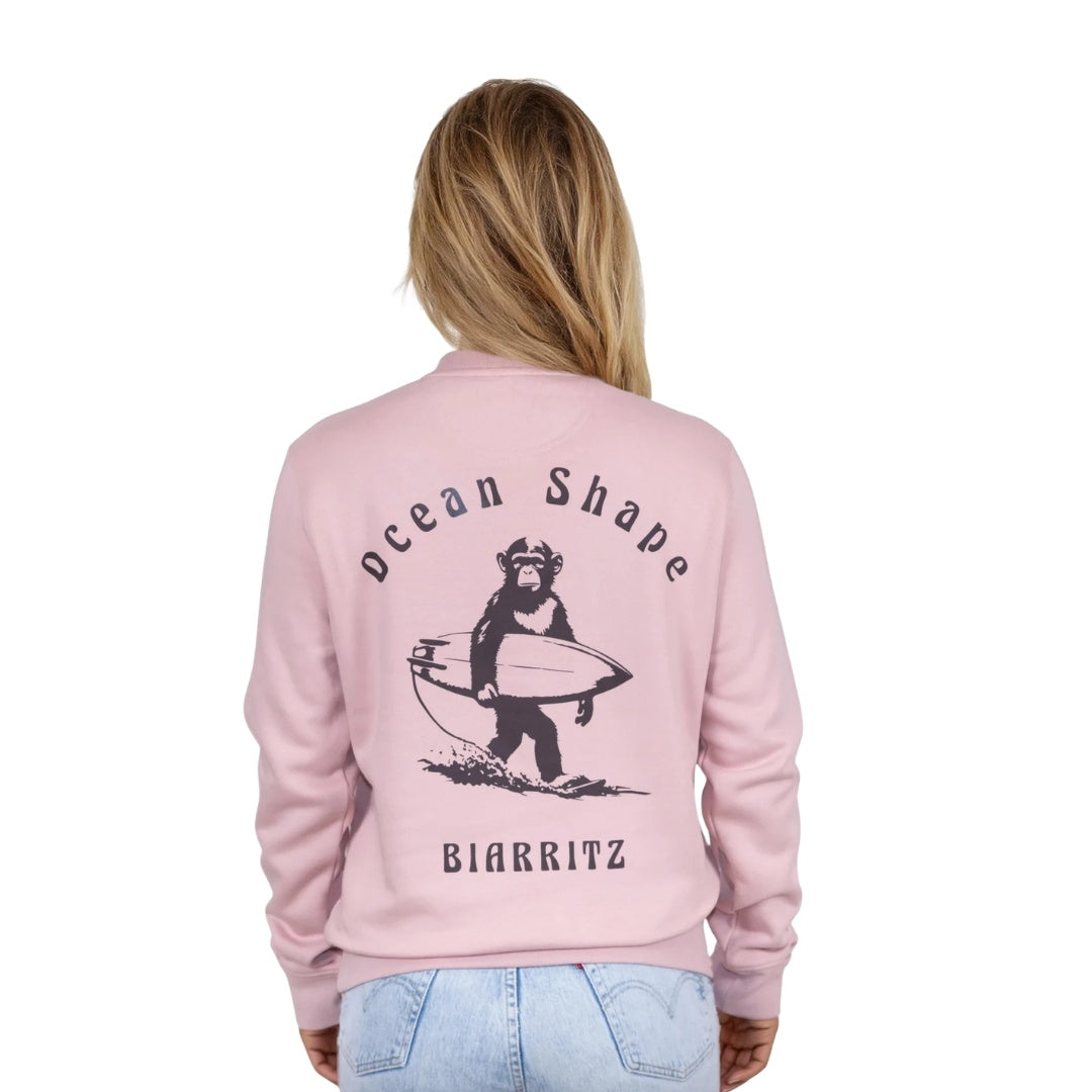 Sweat unisexe rose pale en coton biologique avec gros dessin de singe surfeur et écriture « ocean shape Biarritz » marron foncé dans le dos, vu de dos sur mannequin femme.