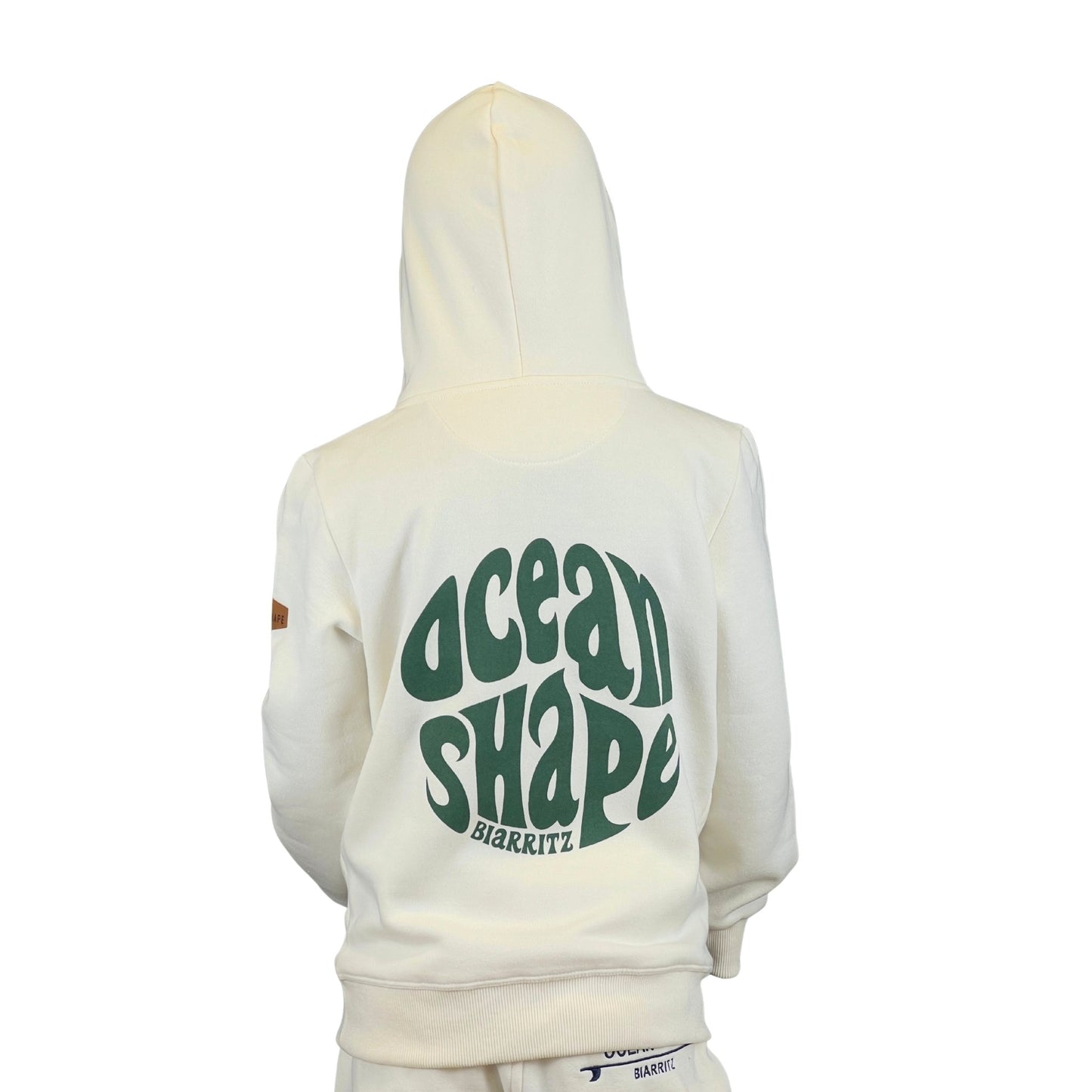 sweat à capuche unisexe ocean shape couleur écru et vert en coton biologique, sur un mannequin enfant de dos.
Dos : grand logo bubble vert avec écriture "biarritz"
