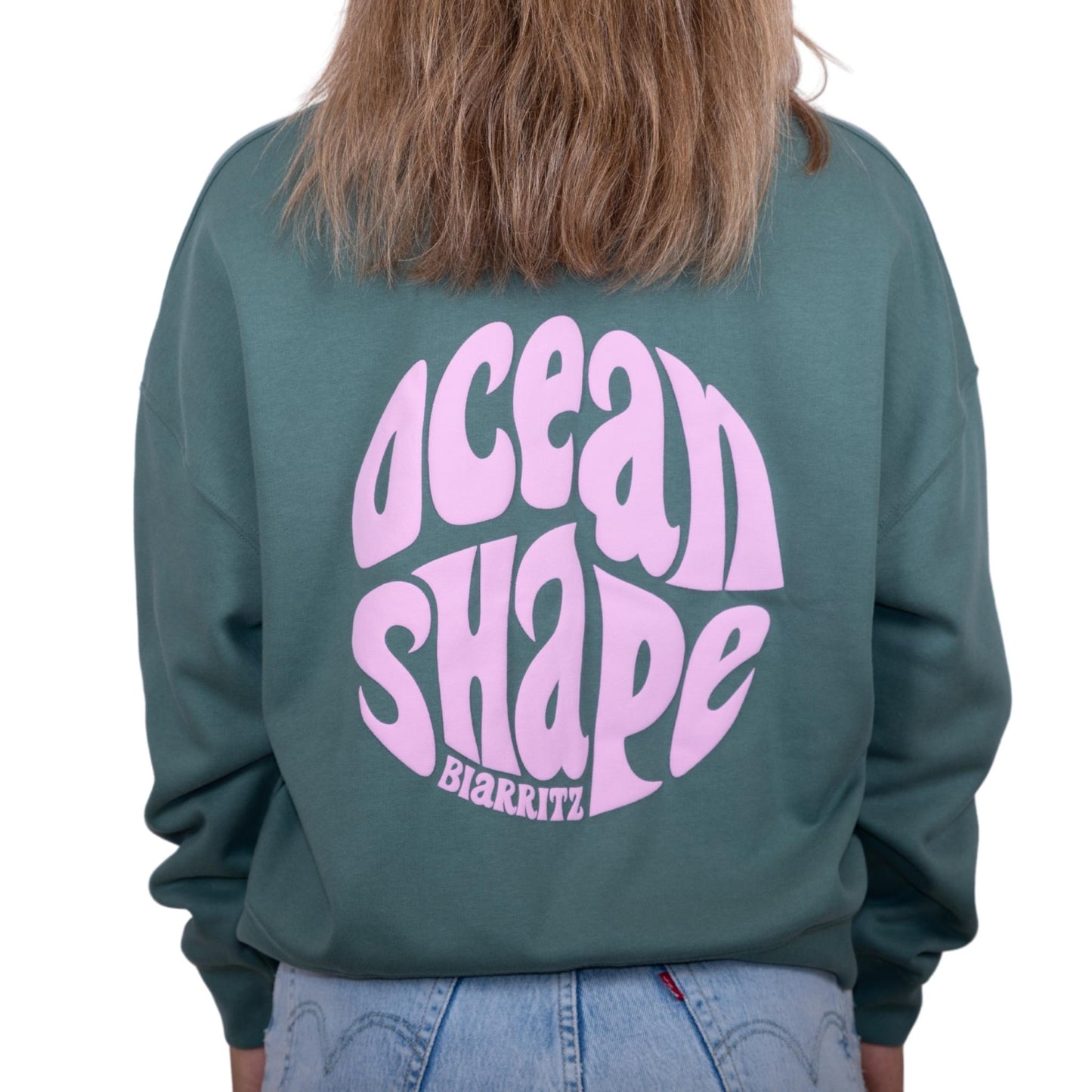 Sweat femme sans capuche vert sauge avec gros logo bubble "ocean shape biarritz" rose pâle dans le dos, vu de dos sur mannequin femme.