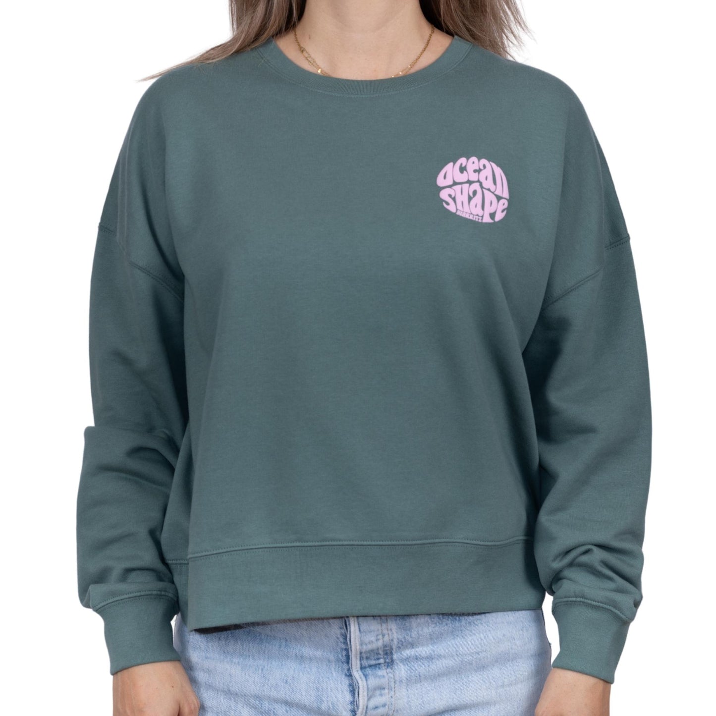 Sweat femme sans capuche vert sauge avec petit logo bubble "ocean shape biarritz" rose pâle sur la poitrine, vu de face sur mannequin femme