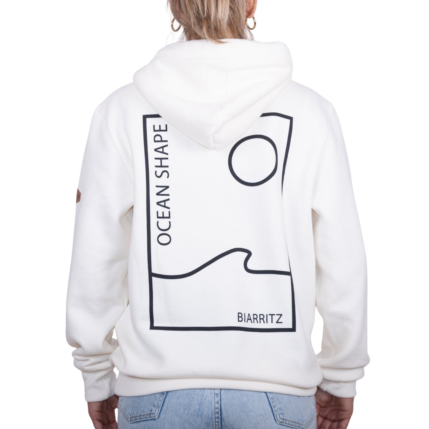 Sweat unisexe à capuche écru avec grand encadré vague / soleil minimaliste + écriture "Ocean Shape Biarritz" noir dans le dos, vu de dos sur mannequin femme