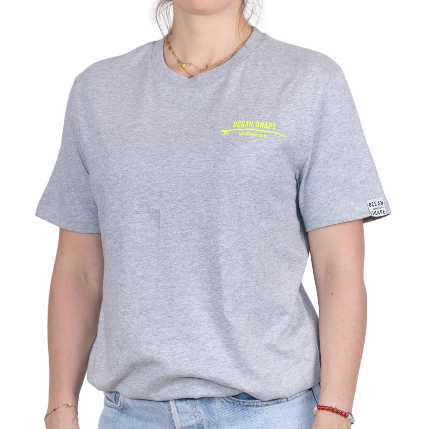 Tee-shirt unisexe gris clair en coton biologique avec petite écriture "ocean shape" jaune fluo sur la poitrine, vu de face sur mannequin femme