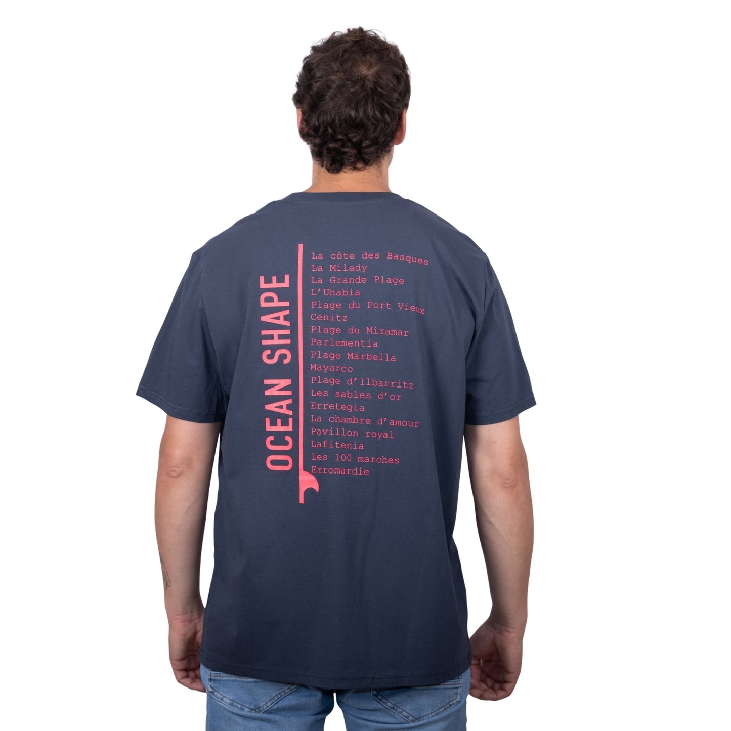 Tee-shirt unisexe gris foncé en coton biologique avec longue liste de plages et grande écriture "ocean shape" rose fluo dans le milieu du dos, vu de dos sur mannequin homme