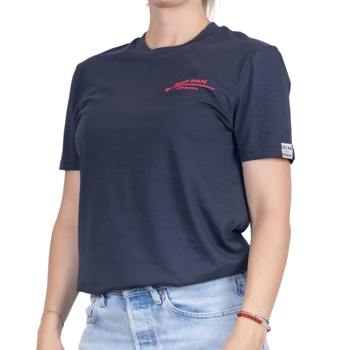 Tee-shirt unisexe gris foncé en coton biologique avec petite écriture "ocean shape" rose fluo sur la poitrine, vu de face sur mannequin femme