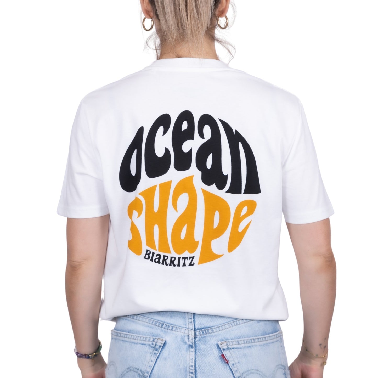 Tee-shirt unisexe blanc en coton biologique avec gros logo ocean shape Biarritz bubble noir et moutarde en haut du dos, vu de dos sur mannequin femme