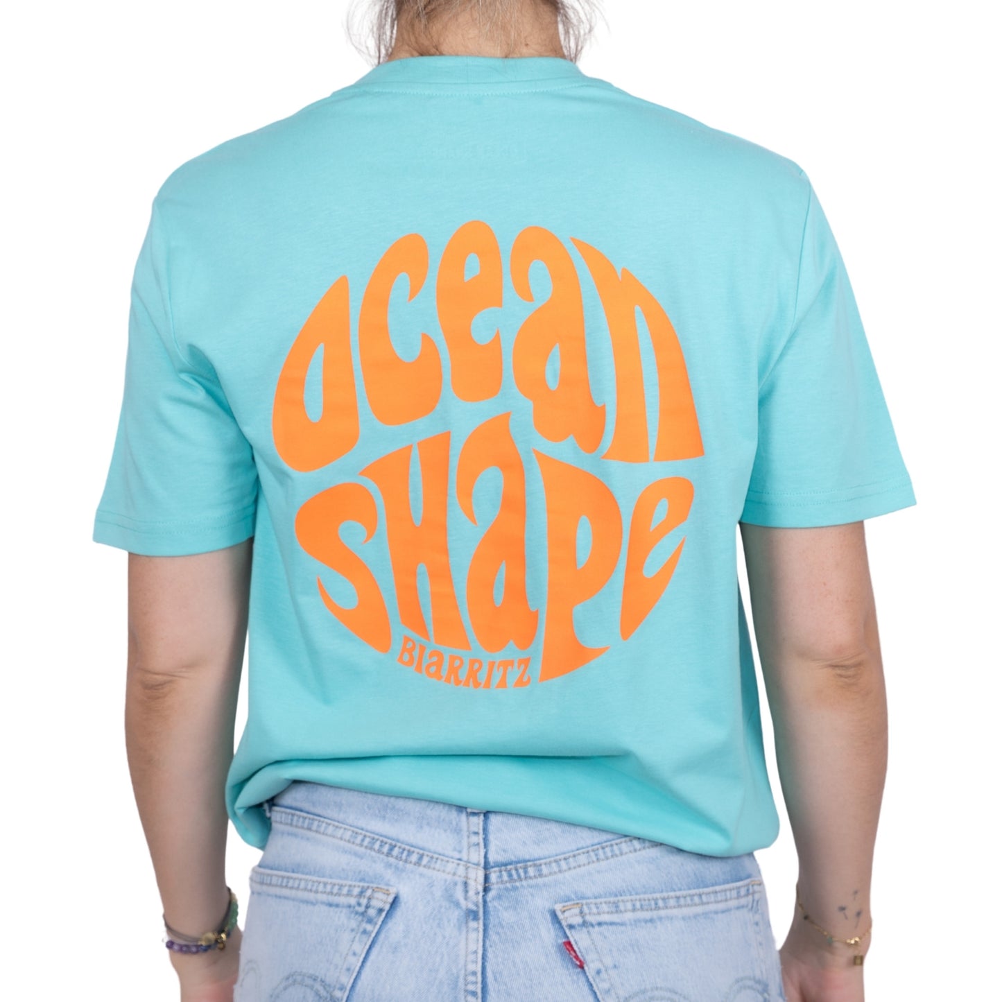 Tee-shirt unisexe bleu ciel en coton biologique avec gros logo ocean shape Biarritz bubble orange fluo en haut du dos, vu de dos sur mannequin femme