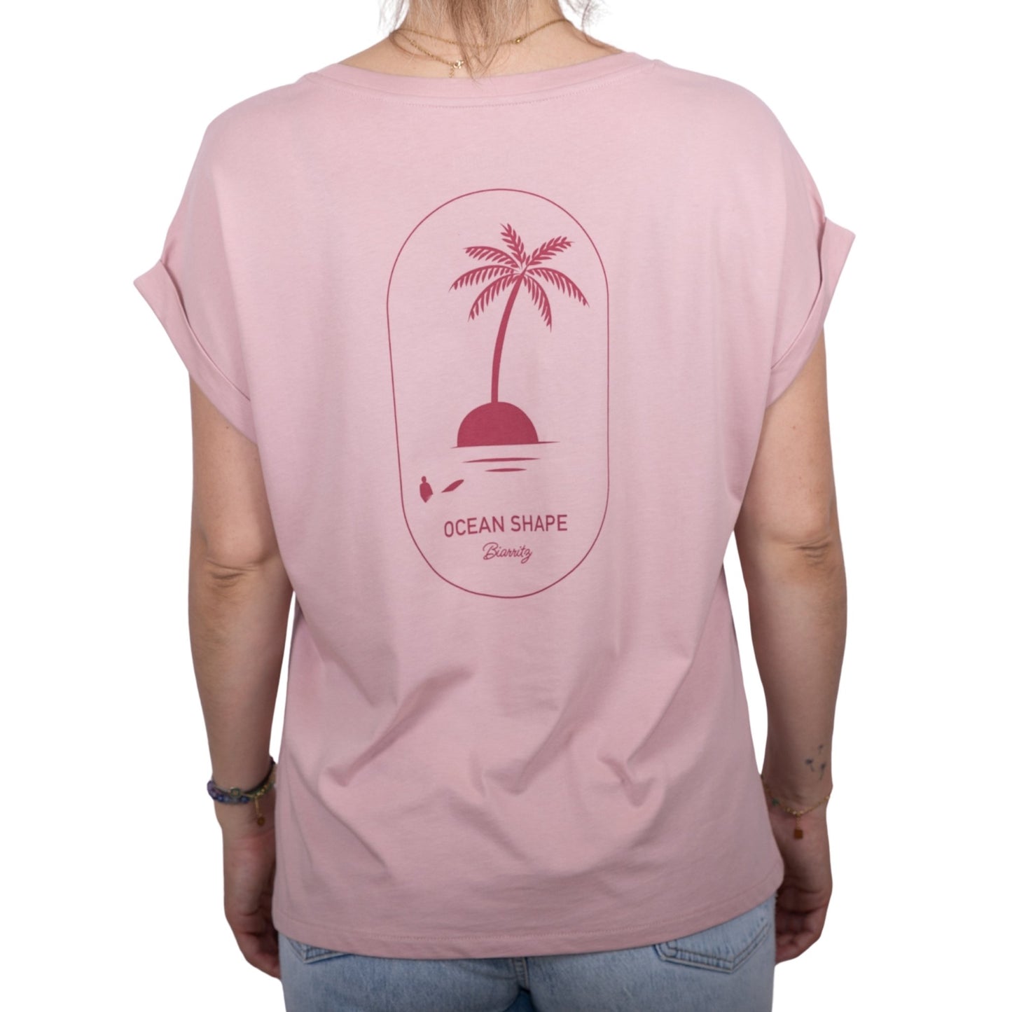 Tee-shirt femme en coton biologique rose pale avec gros dessin palmier sur île et écriture « ocean shape Biarritz » couleur framboise dans le haut du dos, vu de dos sur mannequin femme