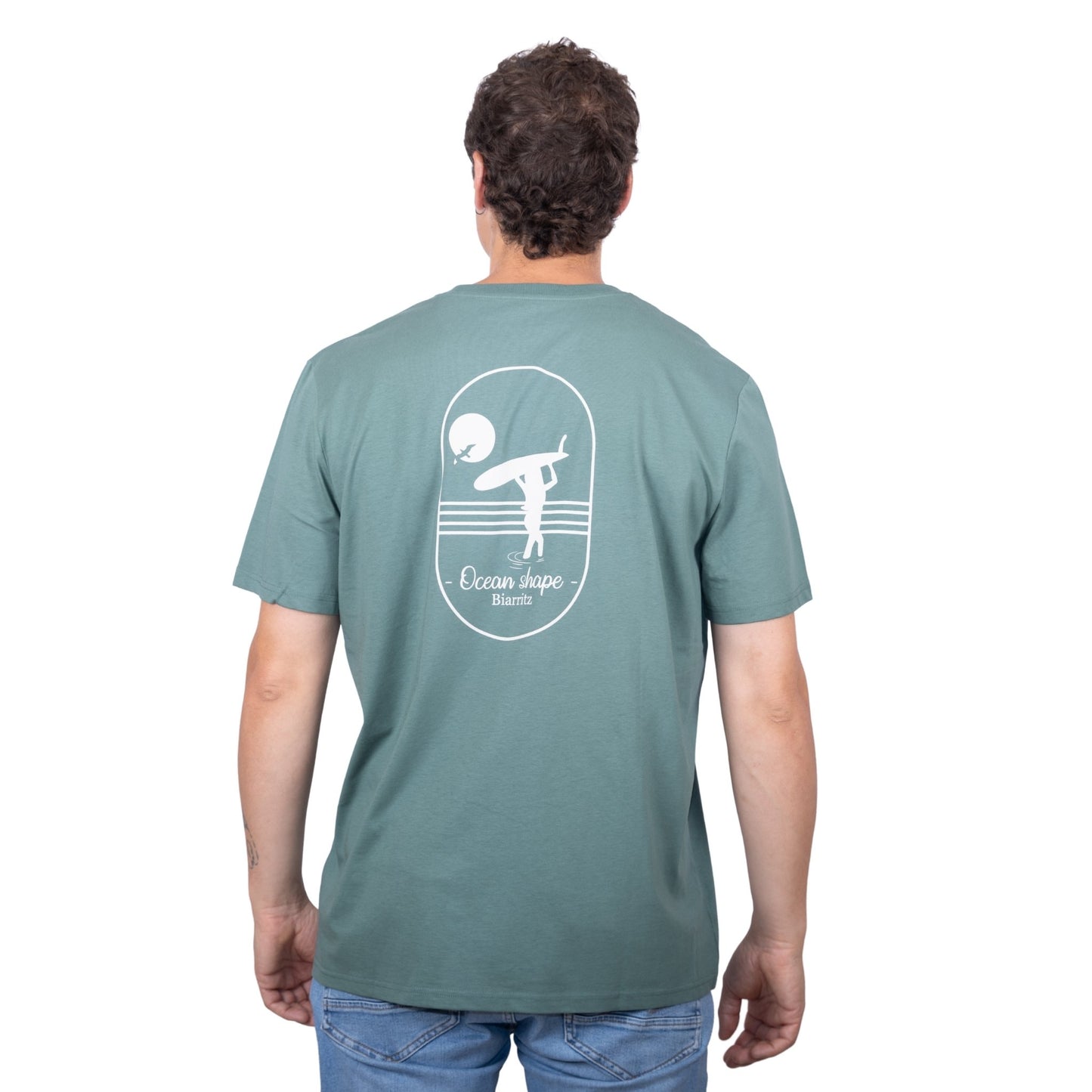 Tee-shirt unisexe vert sauge en coton biologique avec grand dessin de surfeuse qui marche de dos + écriture "Ocean Shape Biarritz" dans le dos, vu de dos sur mannequin homme