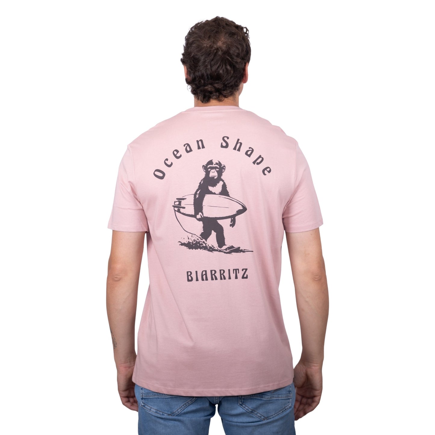 Tee-shirt unisexe rose pale en coton biologique avec gros dessin de singe surfeur et écriture « ocean shape Biarritz » marron foncé dans le dos, vu de dos sur mannequin homme