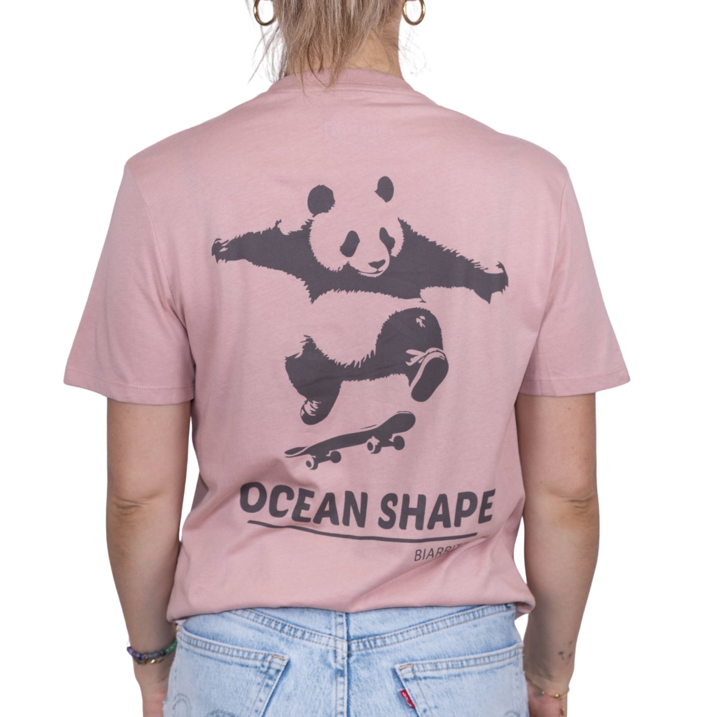T-shirt unisexe rose pale en coton biologique avec gros dessin de panda skateur et écriture « ocean shape Biarritz » marron foncé dans le dos, vue de dos sur mannequin femme