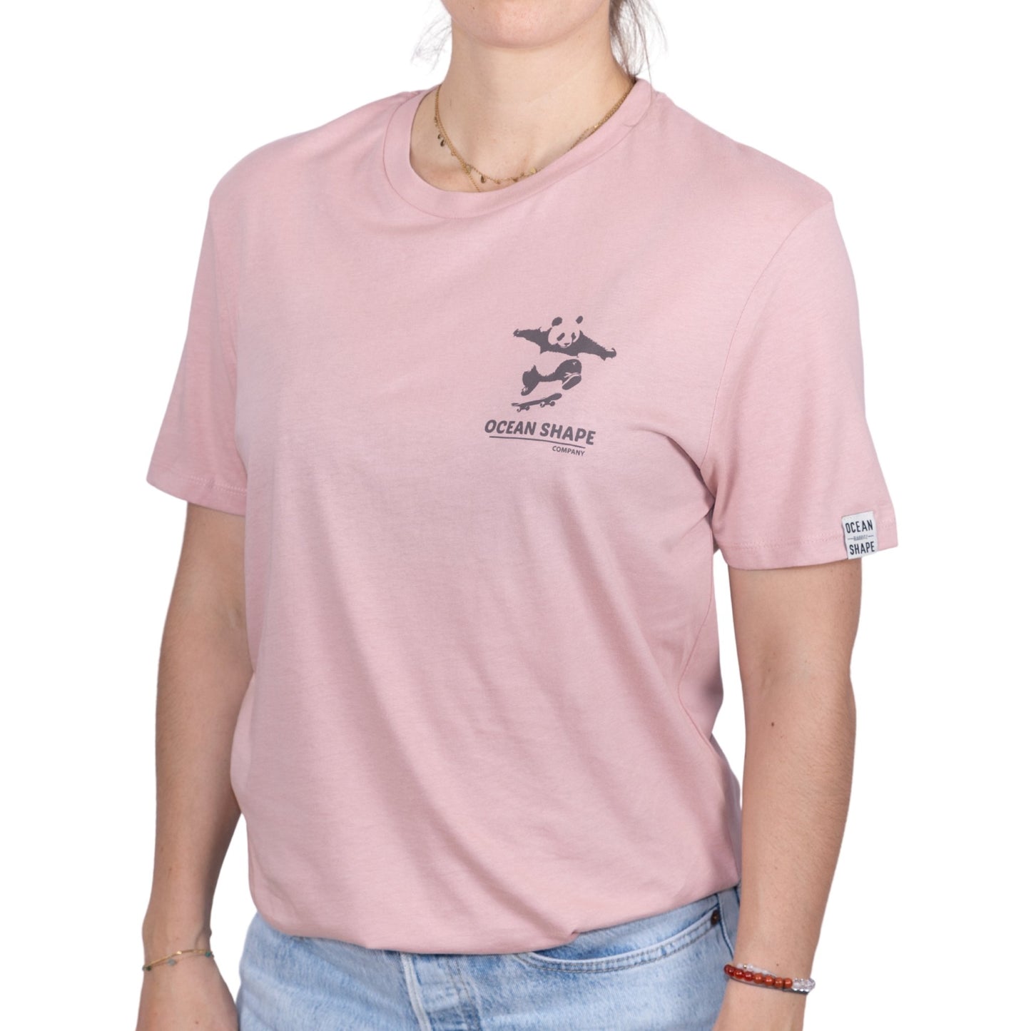T-shirt unisexe rose pale en coton biologique avec petit dessin panda skateur marron foncé sur la poitrine, vue de face sur mannequin femme