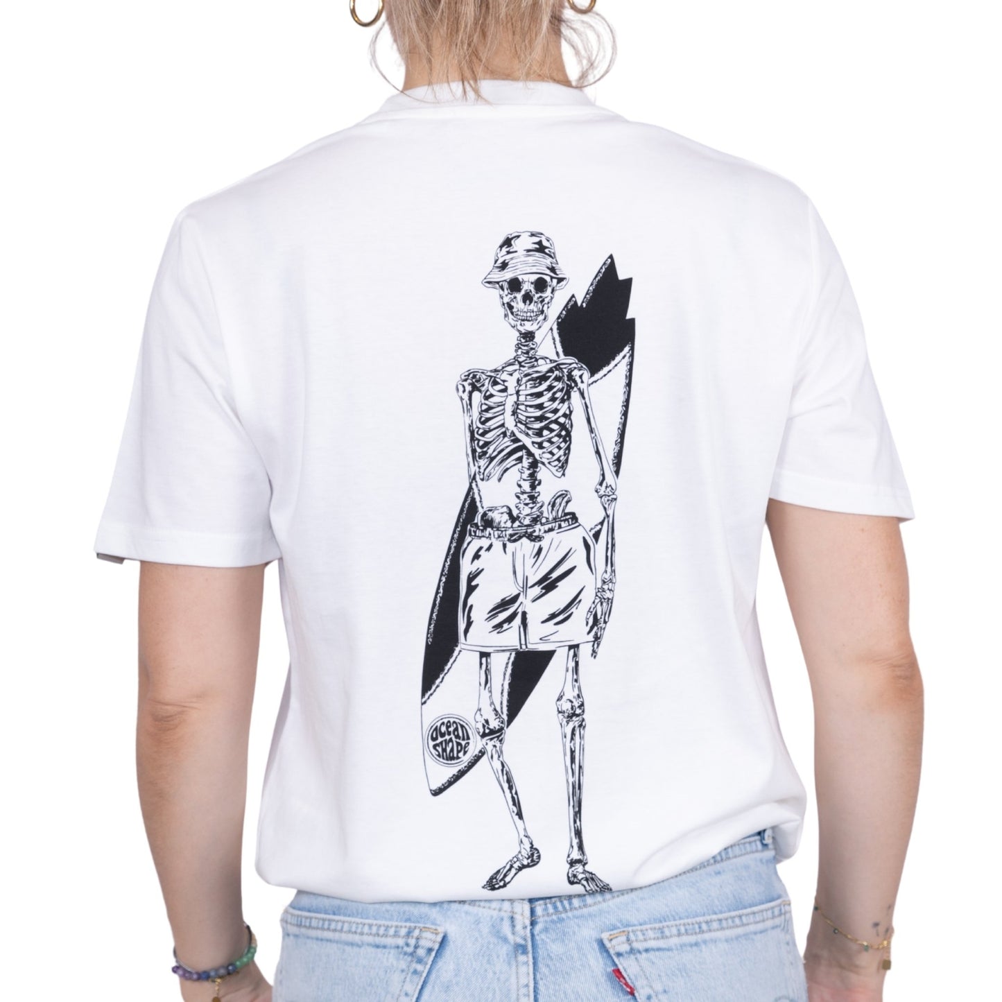 T-shirt unisexe en coton biologique blanc avec gros dessin noir de squelette surfeur dans le dos, vu de dos sur mannequin femme