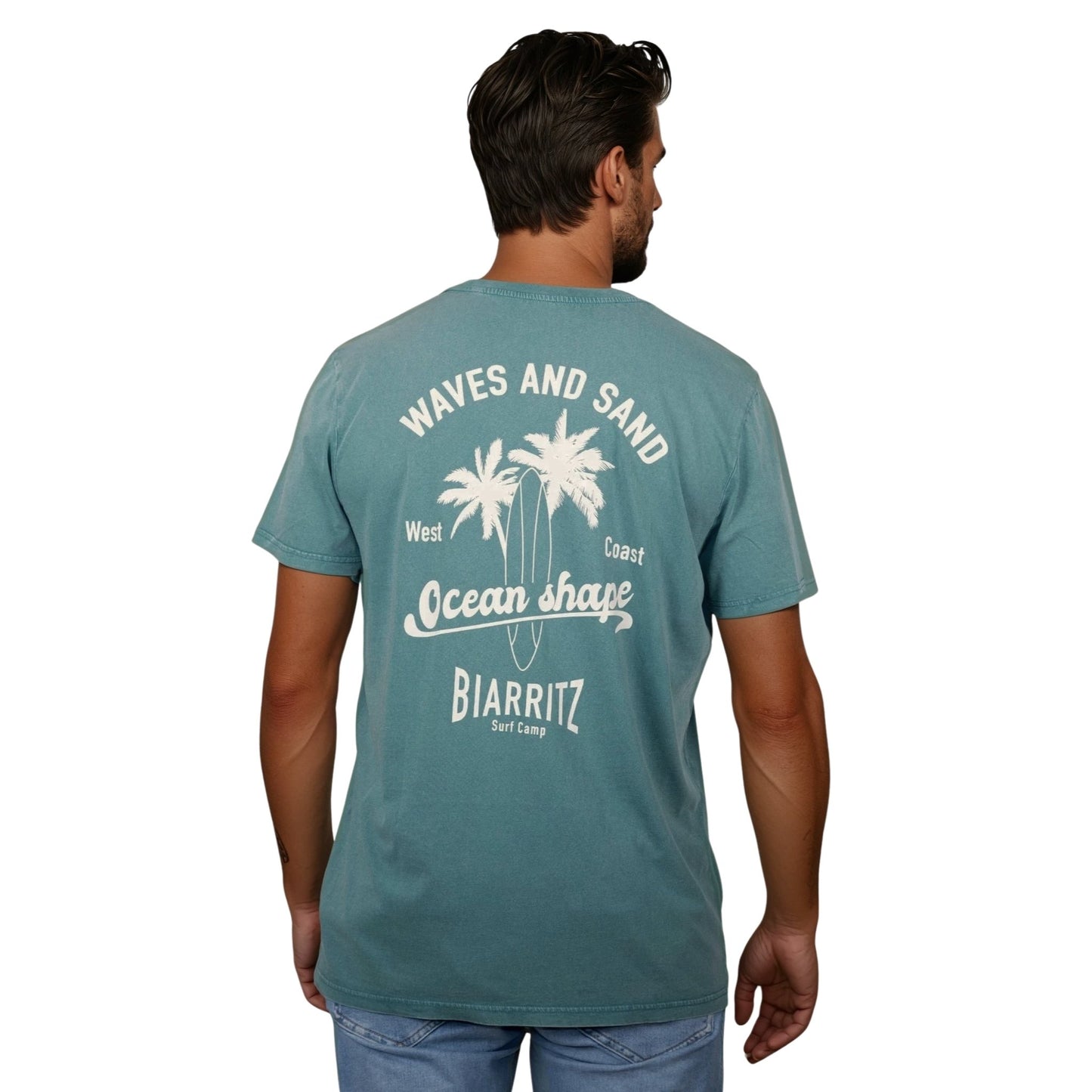 T-shirt unisexe en coton biologique vert sauge délavé avec grand dessin de palmiers, planche de surf et écriture « Waves and sand » et « Ocean Shape Biarritz » écru dans le dos, vu de dos sur mannequin homme.