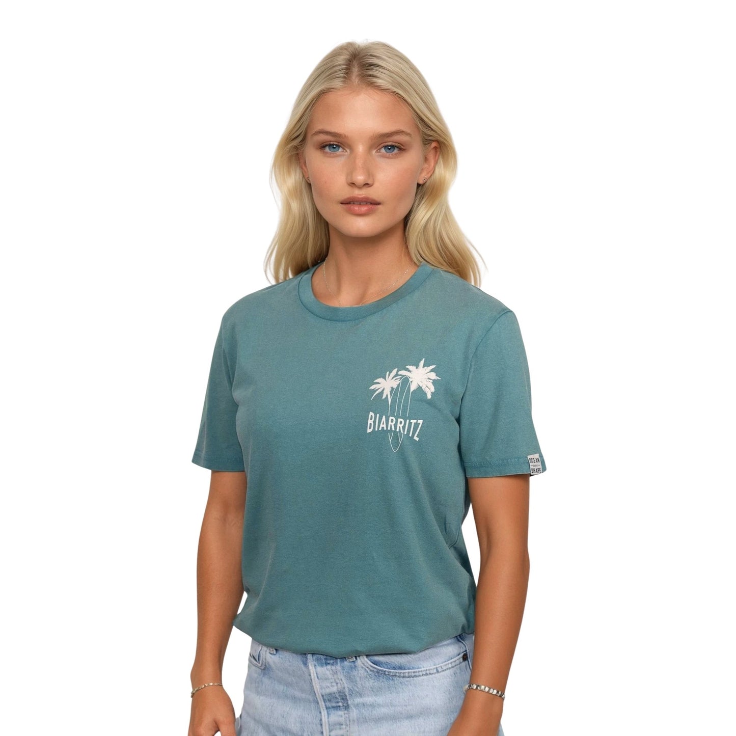T-shirt unisexe en coton biologique vert sauge délavé avec petit dessin palmiers, planche de surf et écriture "Biarritz" écru sur la poitrine, vu de face sur mannequin femme.