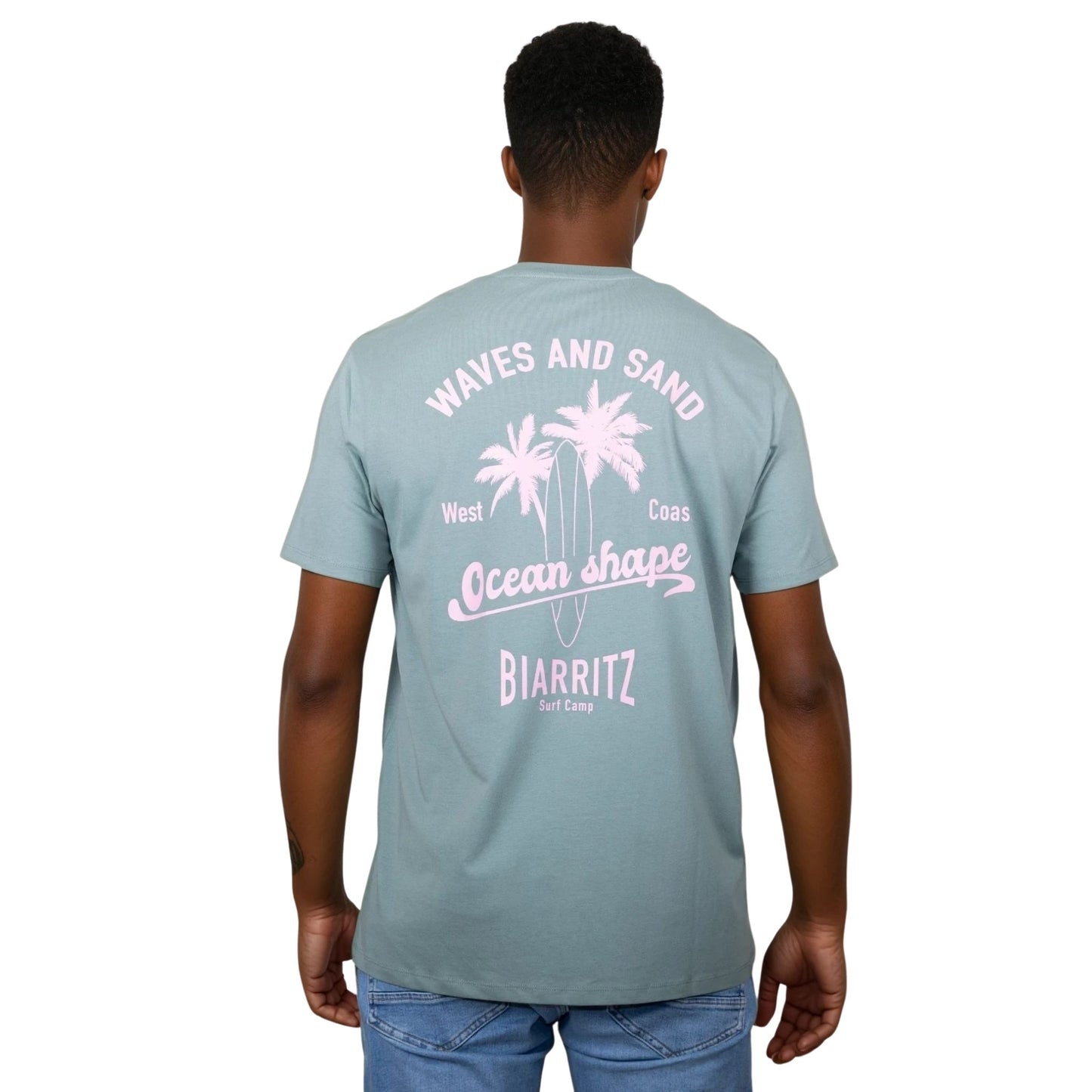 Tee-shirt unisexe vert sauge en coton biologique avec grand dessin de palmiers, planche de surf et écriture "Waves and Sand" et "Ocean Shape Biarritz" rose clair dans le dos, vu de dos sur mannequin homme.