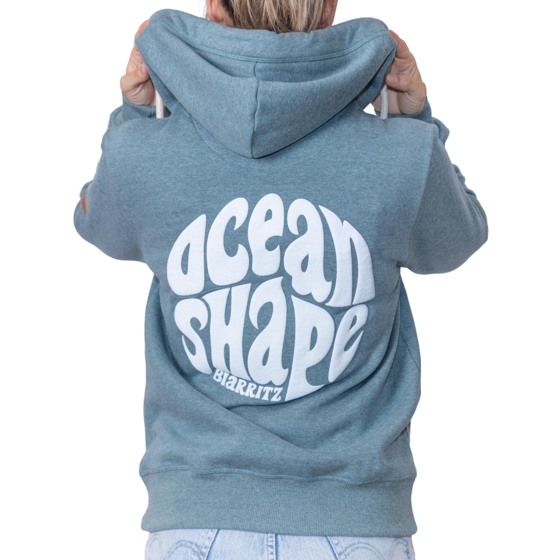Sweat unisexe à capuche vert emeraude avec gros logo bubble "Ocean Shape Biarritz" ecru dans le dos, vu de dos sur mannequin femme