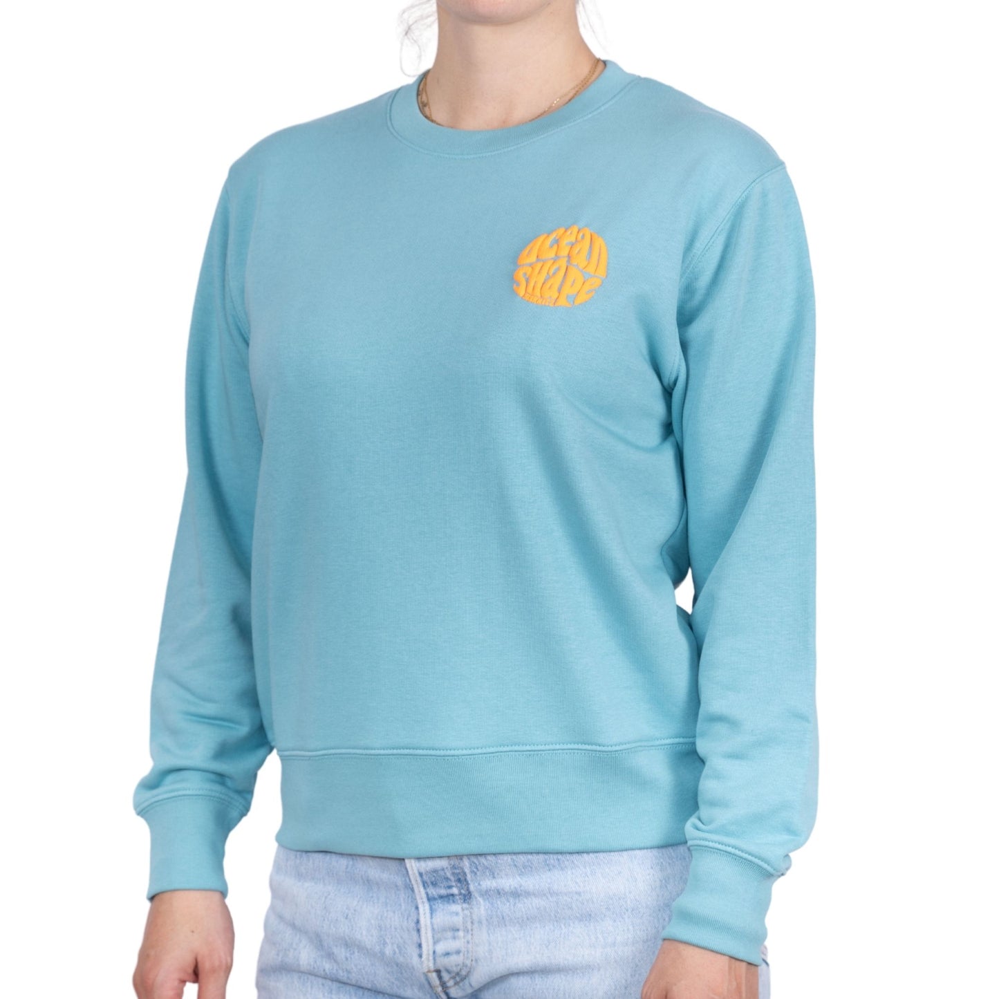 Sweat unisexe sans capuche Teal Monstera avec petit logo bubble "ocean shape biarritz" orange fluo sur la poitrine, vu de face sur mannequin femme.
