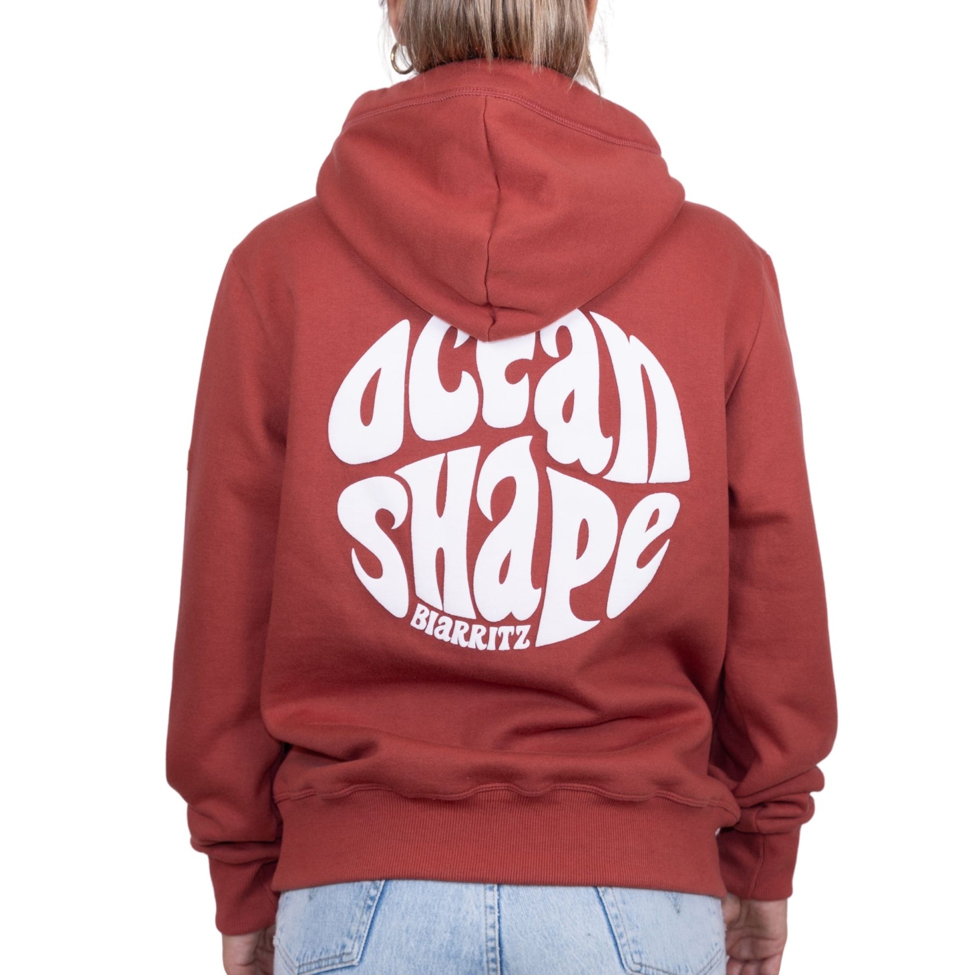 Sweat unisexe à capuche terracotta avec gros logo bubble "Ocean Shape Biarritz" blanc dans le dos, vu de dos sur mannequin femme