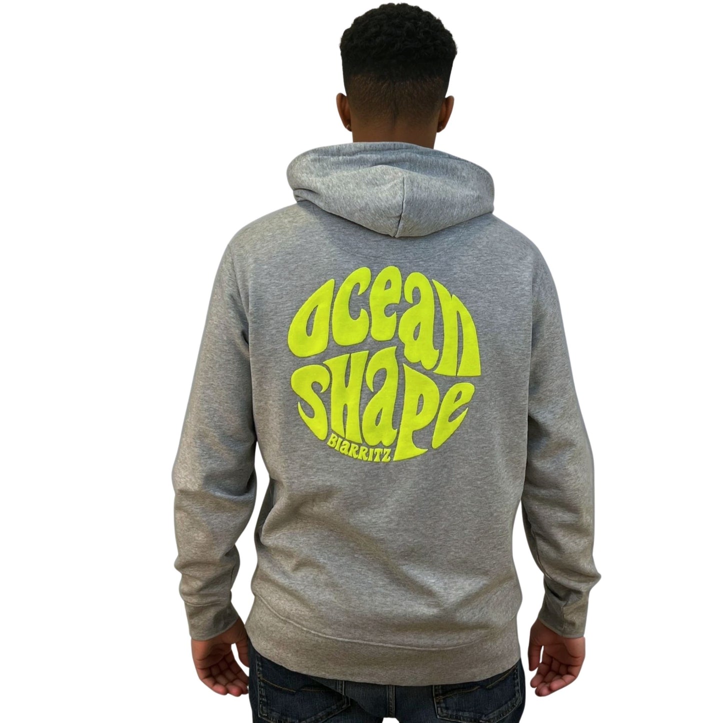 Sweat à capuche unisexe gris.
Gros logo bubble "Ocean Shape Biarritz" en encre gonflante jaune fluo dans le dos.
Vu de dos sur mannequin homme.
