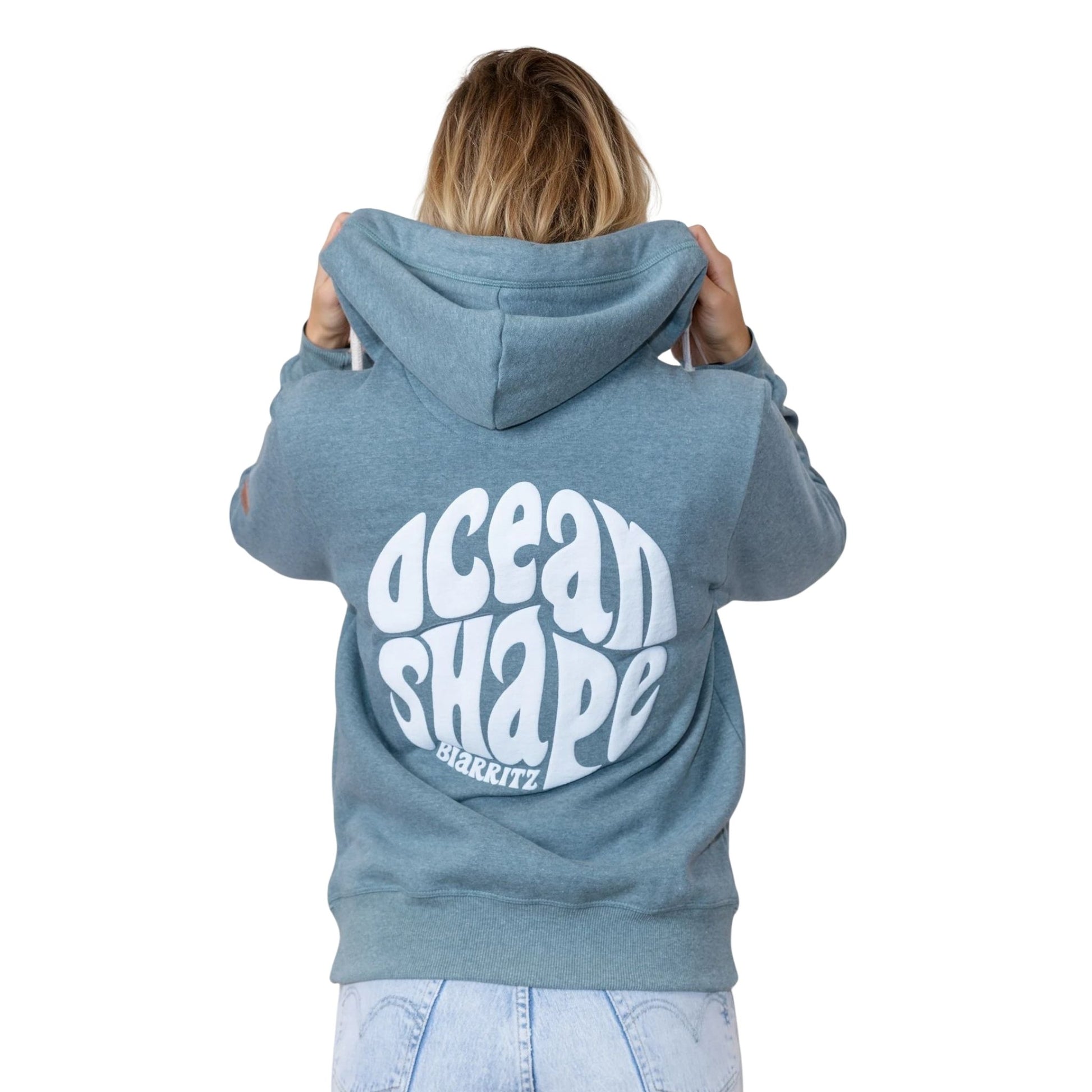 Sweat unisexe à capuche bleu-vert.
Gros logo bubble "Ocean Shape Biarritz" blanc dans le dos.
Vu de dos sur mannequin femme.