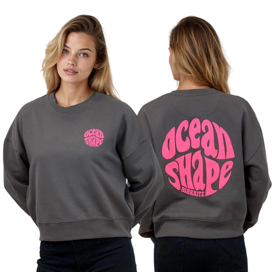 Sweat femme court et oversize, col rond, épaules tombantes, 100 % coton biologique, couleur gris anthracite.
Devant : petit logo bubble "Ocean shape Biarritz" rose fluo sur la poitrine gauche.
Dos : gros logo bubble "Ocean shape Biarritz" rose fluo.
Vu de face et de dos sur mannequin femme.