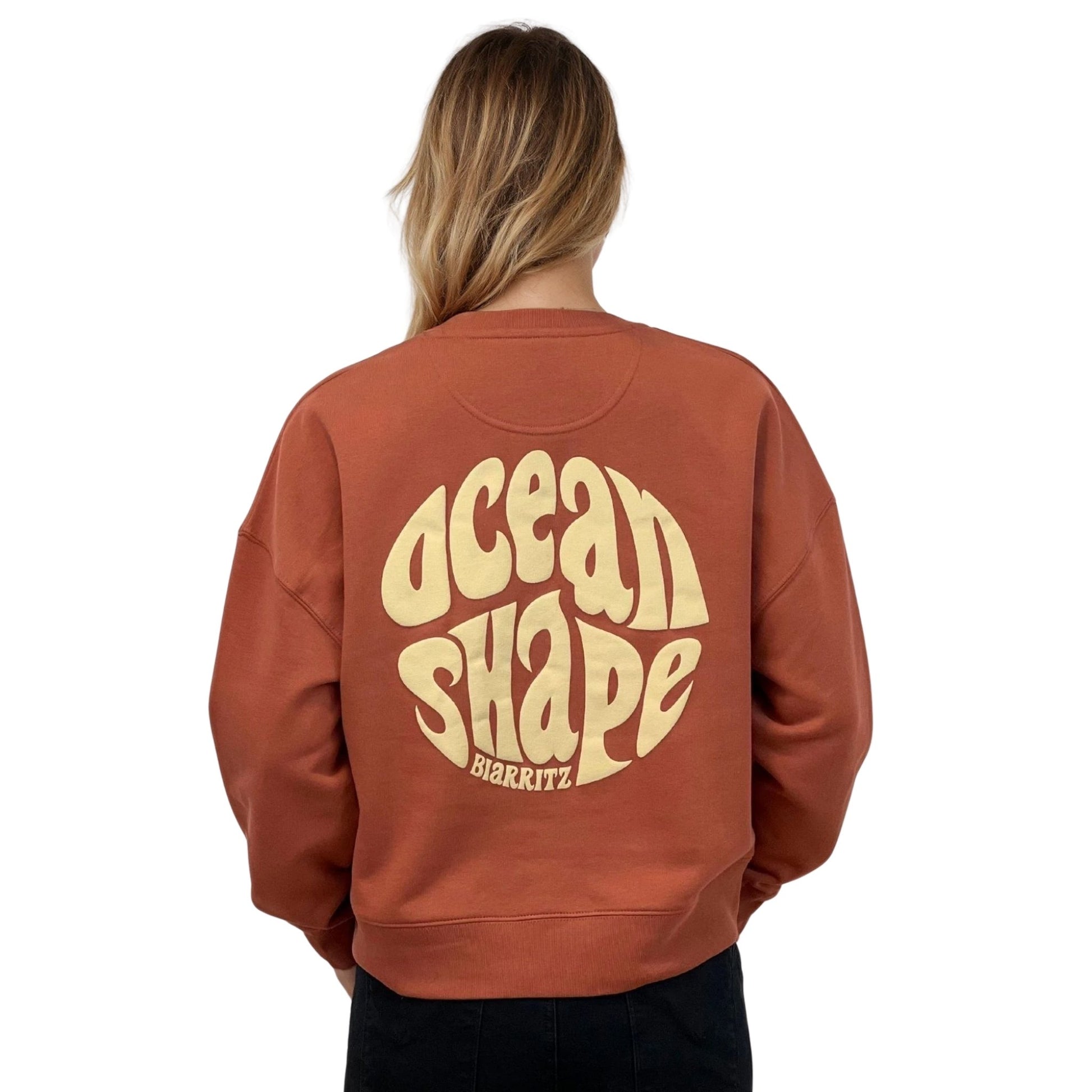 Sweat femme court et oversize, col rond, épaules tombantes, 100 % coton biologique, couleur terracotta.
Gros logo bubble "Ocean shape Biarritz" beige dans le dos.
Vu de dos sur mannequin femme.