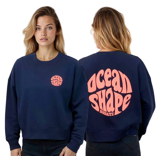 Sweat femme court et oversize, col rond, épaules tombantes, 100 % coton biologique, bleu marine.
Devant : petit logo bubble "Ocean shape Biarritz" corail fluo sur la poitrine gauche.
Dos : gros logo bubble "Ocean shape Biarritz" corail fluo.
Vu de face et de dos sur mannequin femme.