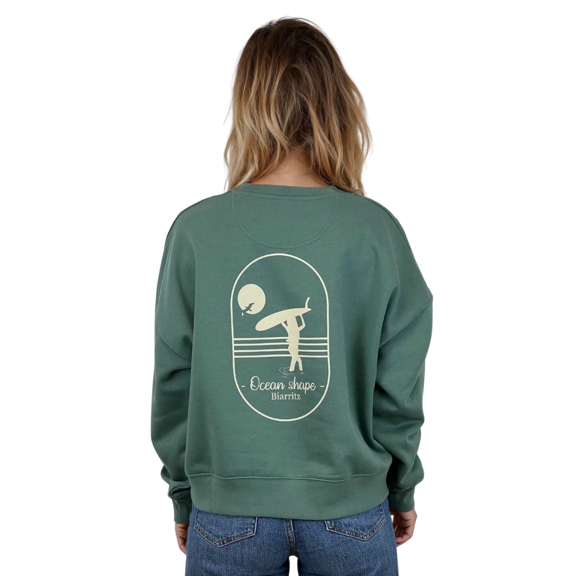 Sweat femme court et oversize, col rond, épaules tombantes, 100 % coton biologique, couleur vert sauge.
Grand dessin beige de surfeuse qui marche avec sa planche sur la tête et écriture Ocean Shape Biarritz dans le dos.
Vu de dos sur mannequin femme.
