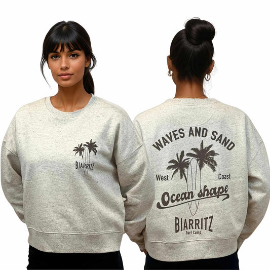 Sweat femme court et oversize, col rond, épaules tombantes, 100 % coton biologique, couleur gris clair chiné.
Devant : petit dessin marron de planche de surf et palmiers + écriture "Biarritz" sur la poitrine gauche.
Dos : grand dessin marron de planche de surf et palmiers + écriture "Waves and sand, Ocean Shape Biarritz".
Vu de face et de dos sur mannequin femme.
