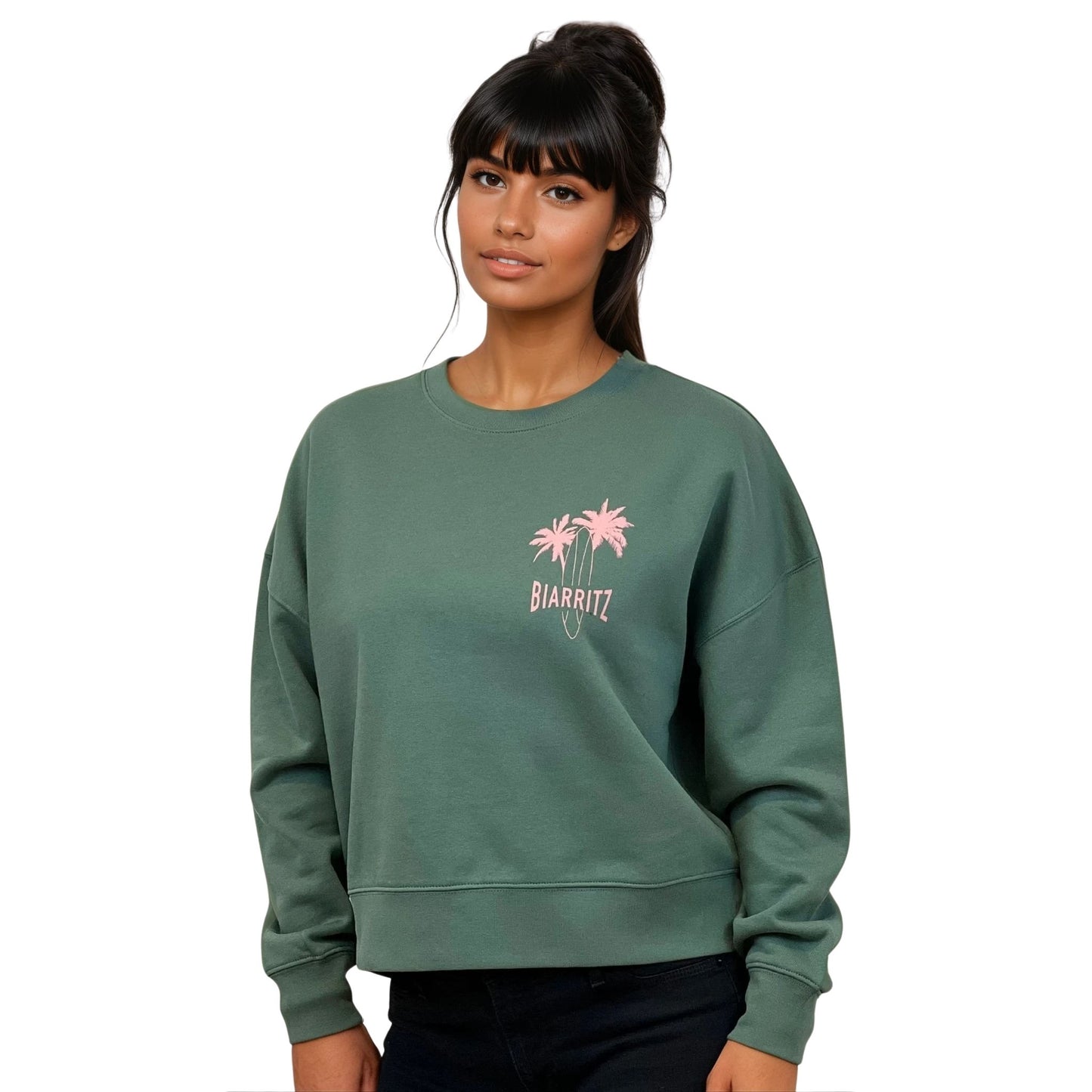 Sweat femme court et oversize, col rond, épaules tombantes, 100 % coton biologique, couleur vert sauge.
Petit dessin rose pâle de planche de surf et palmiers + écriture "Biarritz" sur la poitrine gauche.
Vu de face sur mannequin femme.