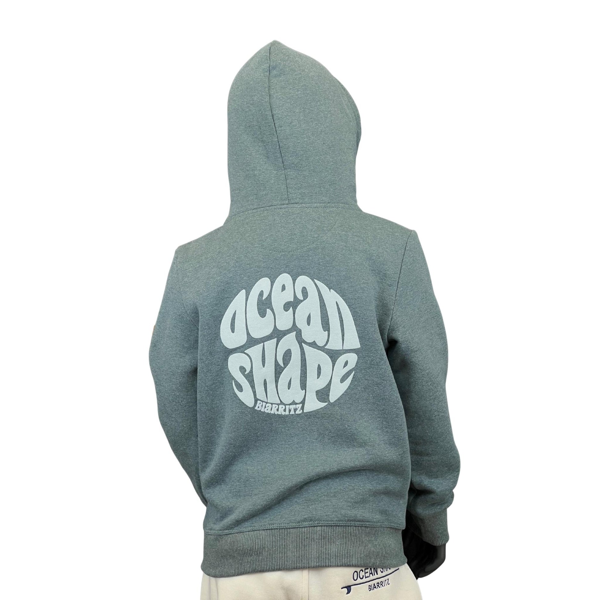 sweat à capuche unisexe enfant de couleur émeraude, vu sur un mannequin enfant de dos.
Dos : logo bubble ocean shape biarritz en relief et en grand dans le dos.
Le mannequin porte également une casquette.