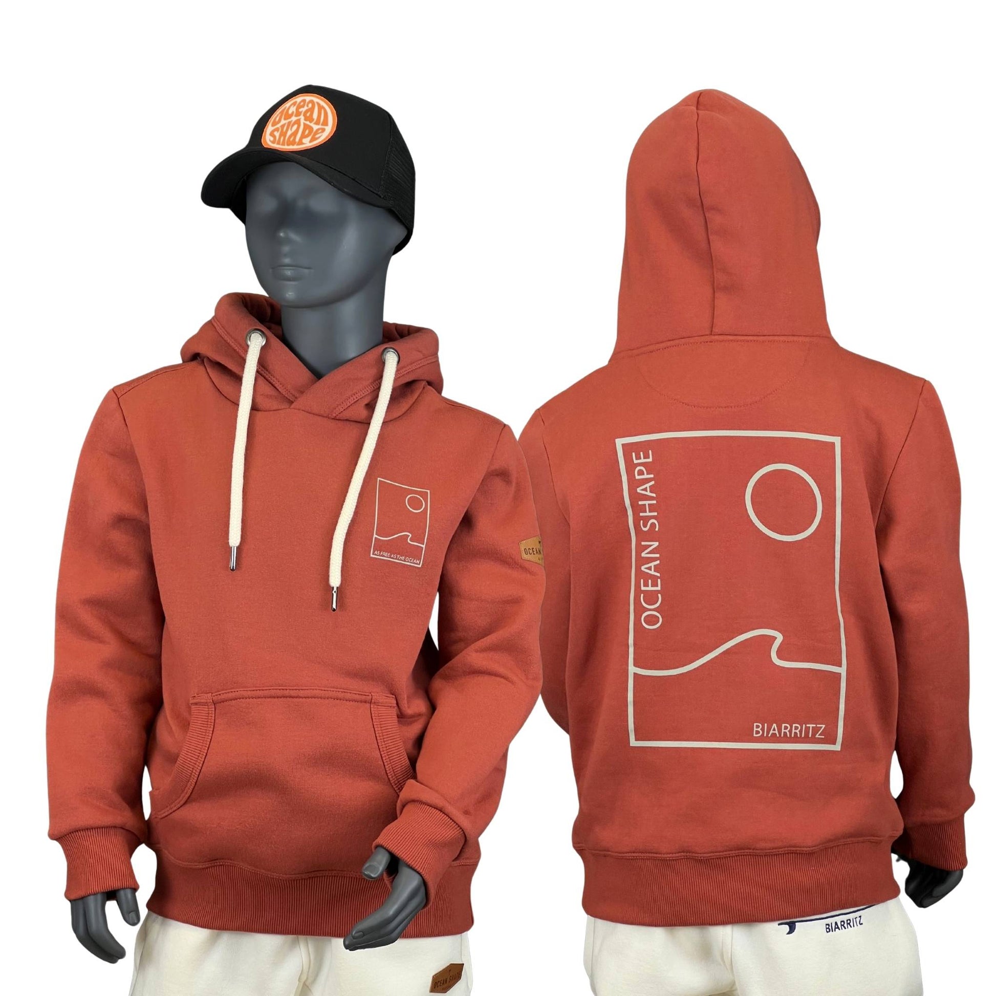 sweat à capuche unisexe enfant de couleur terracotta, vu sur un mannequin enfant de face et de dos.
Devant : logo ocean shape Biarritz en bubble en relief et une poche kangourou.
Dos : logo bubble ocean shape biarritz en relief et en grand dans le dos.
Le mannequin porte également une casquette.