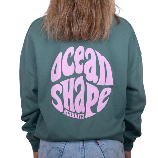 Sweat femme sans capuche vert sauge avec gros logo bubble "ocean shape biarritz" rose pâle dans le dos, vu de dos sur mannequin femme.