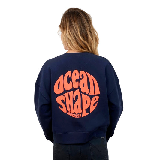 Sweat femme court et oversize, col rond, épaules tombantes, 100 % coton biologique, bleu marine.
Gros logo bubble "Ocean shape Biarritz" corail fluo.
Vu de dos sur mannequin femme.