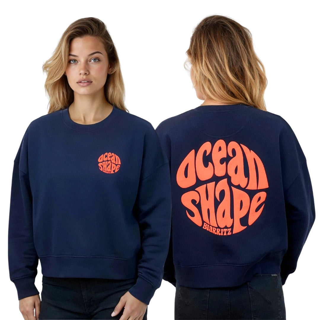Sweat femme court et oversize, col rond, épaules tombantes, 100 % coton biologique, bleu marine.
Devant : petit logo bubble "Ocean shape Biarritz" corail fluo sur la poitrine gauche.
Dos : gros logo bubble "Ocean shape Biarritz" corail fluo.
Vu de face et de dos sur mannequin femme.