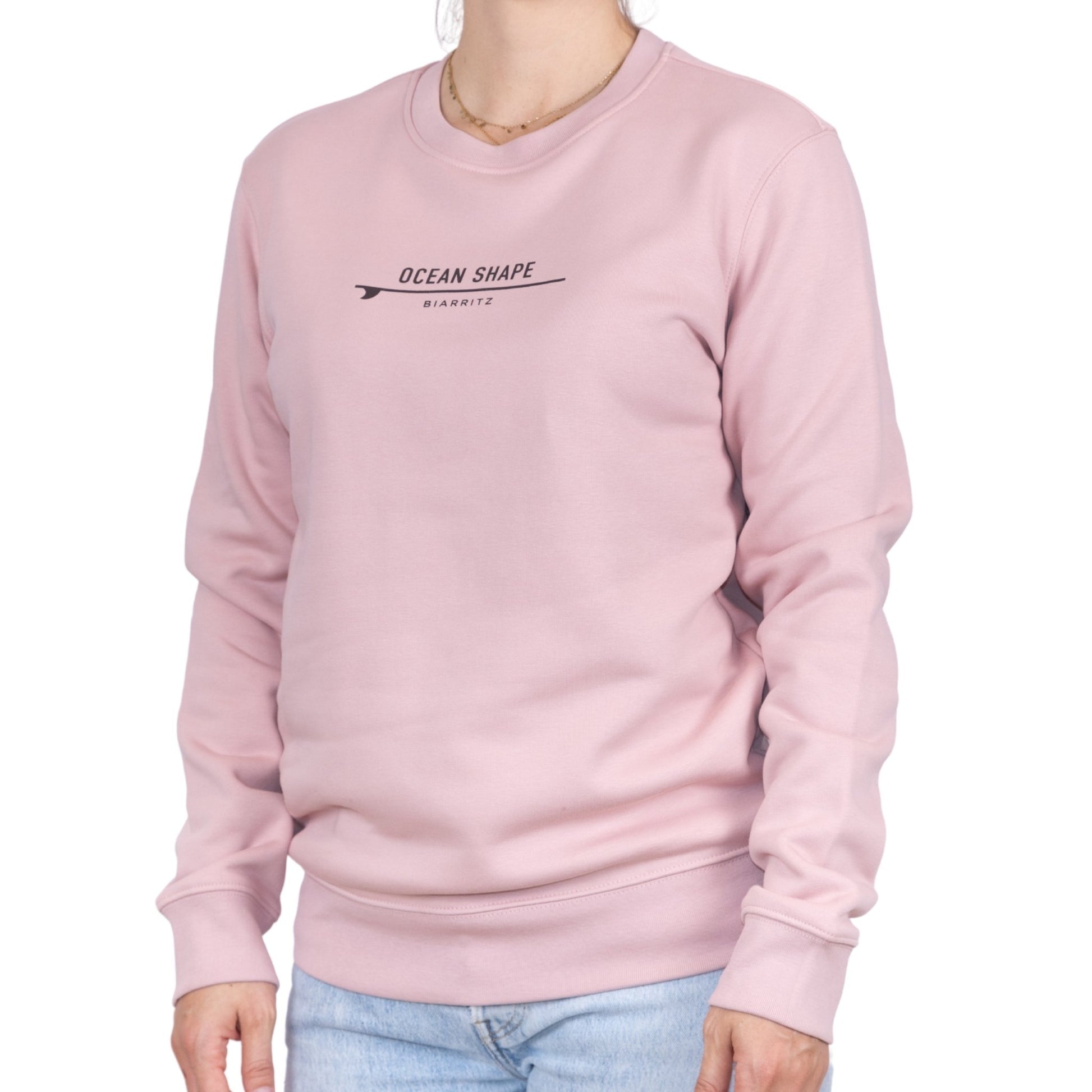 Sweat unisexe rose pale en coton biologique avec petite signature "ocean shape Biarritz" sur surf marron foncé sur la poitrine, vu de face sur mannequin femme.