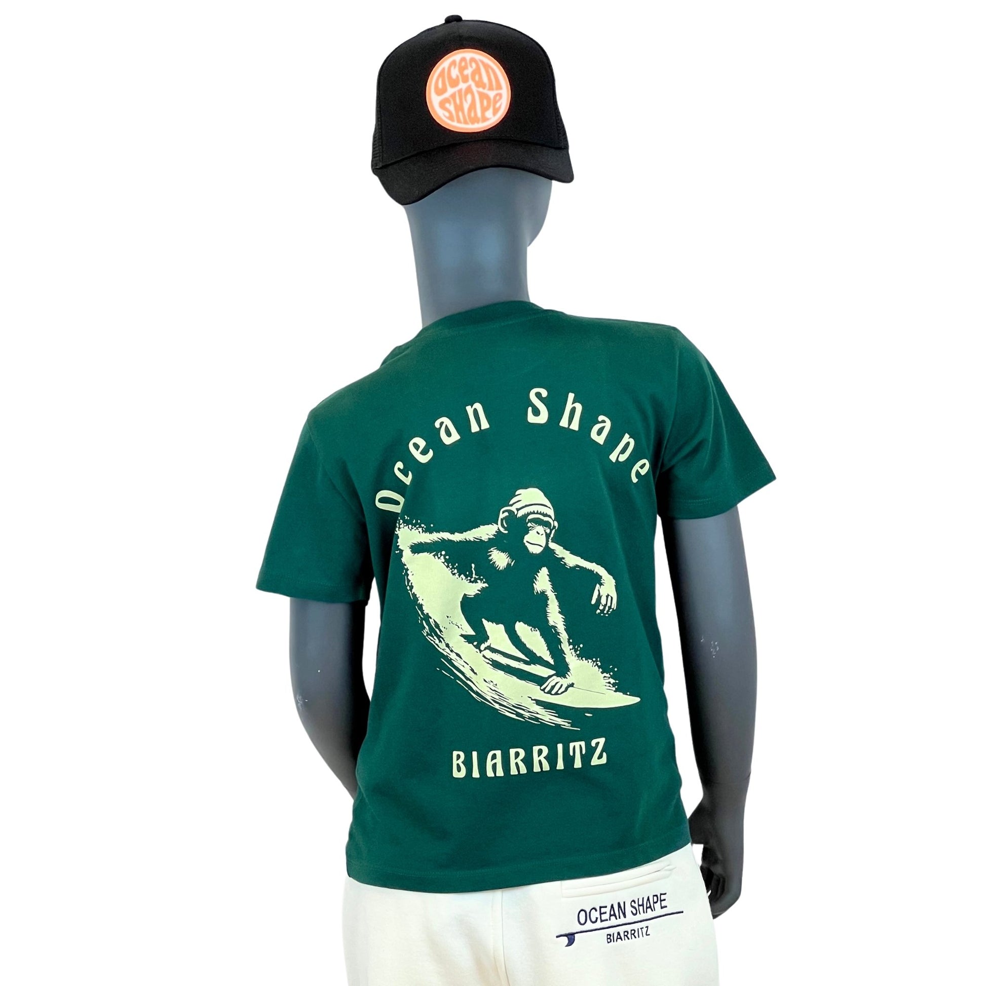 tshirt enfant ocean shape vert foncé, 100% coton biologique.
Illustration beige d'un singe qui fait du surf et écritures "ocean shape, biarritz".
Vu de dos sur mannequin enfant.