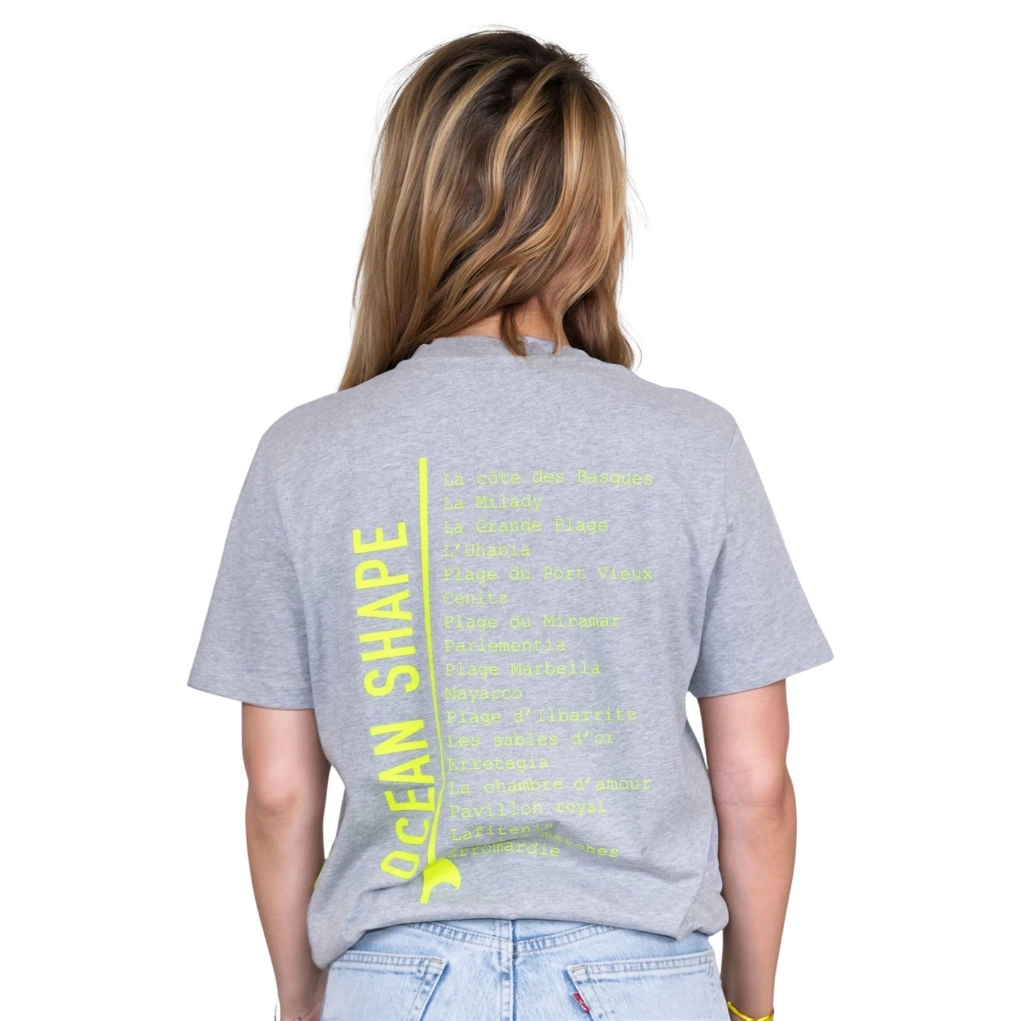 Tee-shirt unisexe gris clair en coton biologique avec longue liste de plages et grande écriture "ocean shape" jaune fluo dans le milieu du dos, vu de dos sur mannequin femme