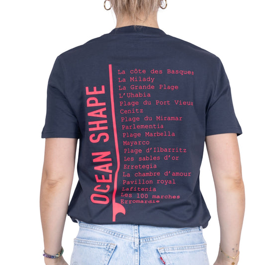 Tee-shirt unisexe gris foncé en coton biologique avec longue liste de plages et grande écriture "ocean shape" rose fluo dans le milieu du dos, vu de dos sur mannequin femme