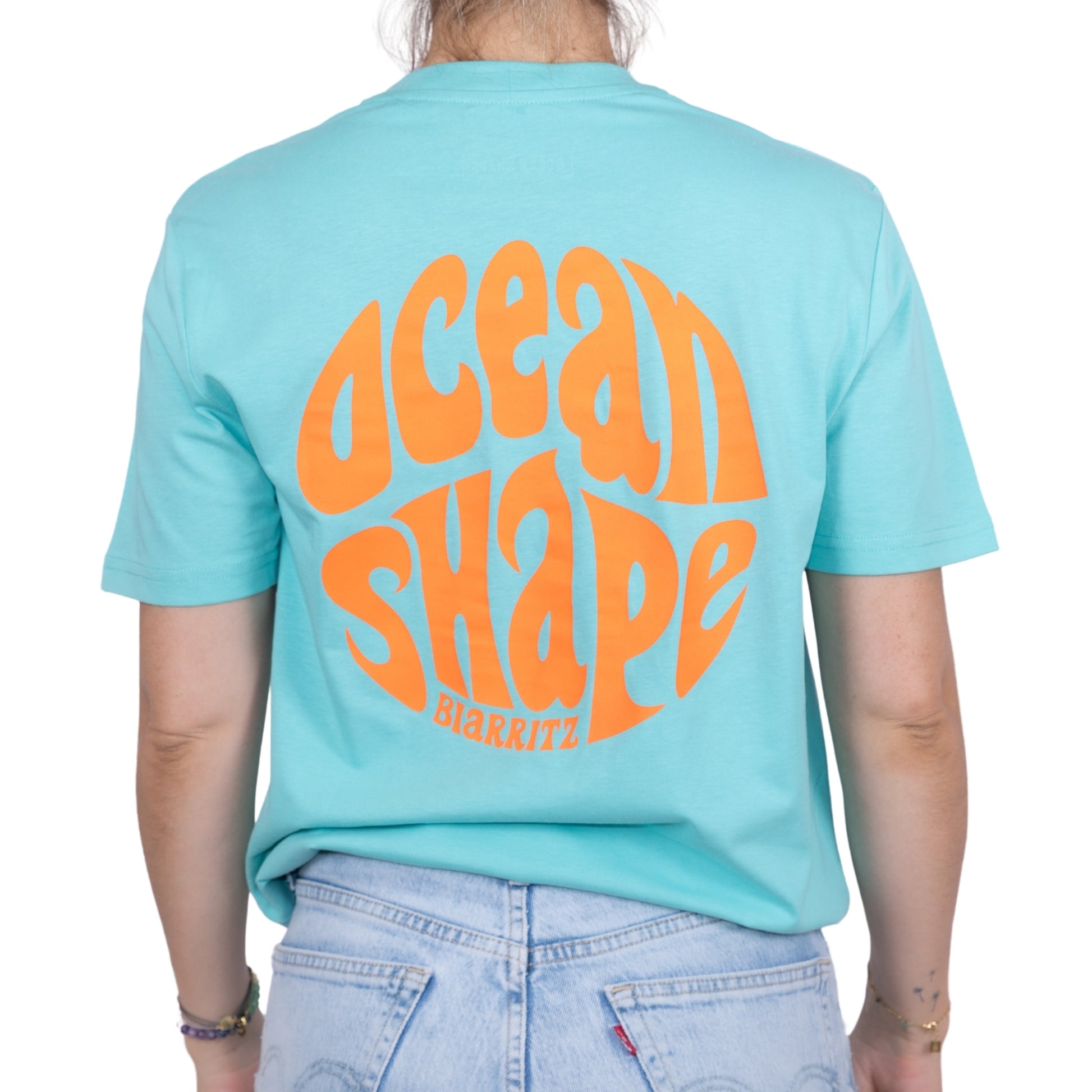 Tee-shirt unisexe bleu ciel en coton biologique avec gros logo ocean shape Biarritz bubble orange fluo en haut du dos, vu de dos sur mannequin femme