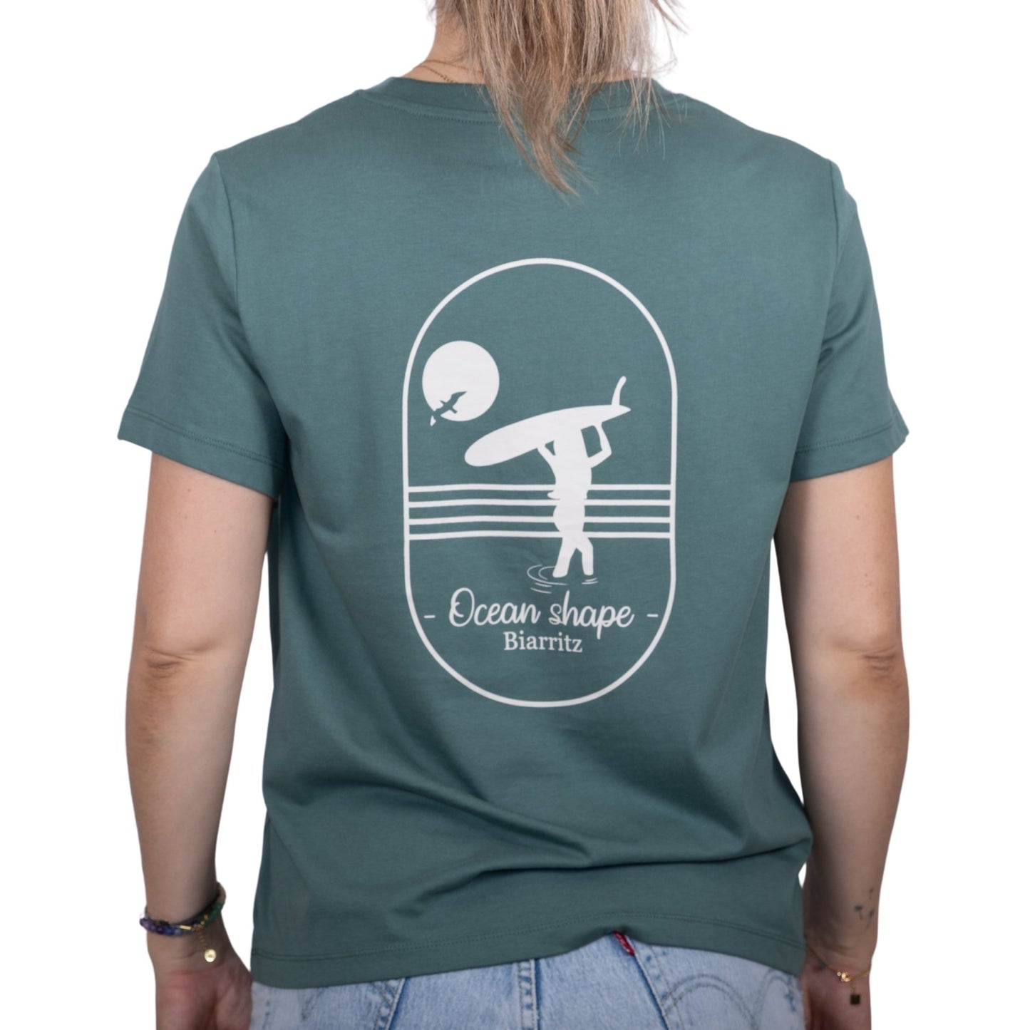 Tee-shirt femme en coton biologique vert sauge avec gros dessin surfeuse qui marche de dos et écriture ocean shape Biarritz écru dans le dos , vu de dos sur mannequin femme 