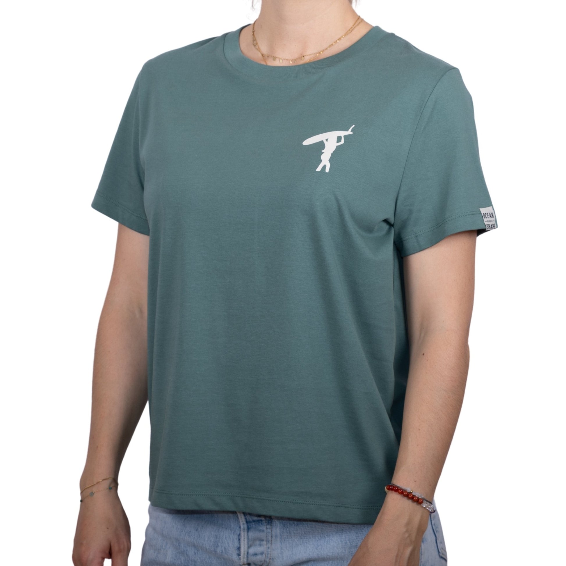 Tee-shirt femme en coton biologique vert sauge avec petit dessin de surfeuse qui marche de dos en écru sur la poitrine, vu de face sur mannequin femme 