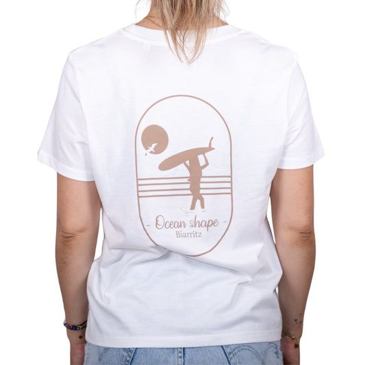 Tee-shirt femme en coton biologique blanc avec gros dessin de surfeuse qui marche de dos et écriture "ocean shape Biarritz" beige dans le dos , vu de dos sur mannequin femme
