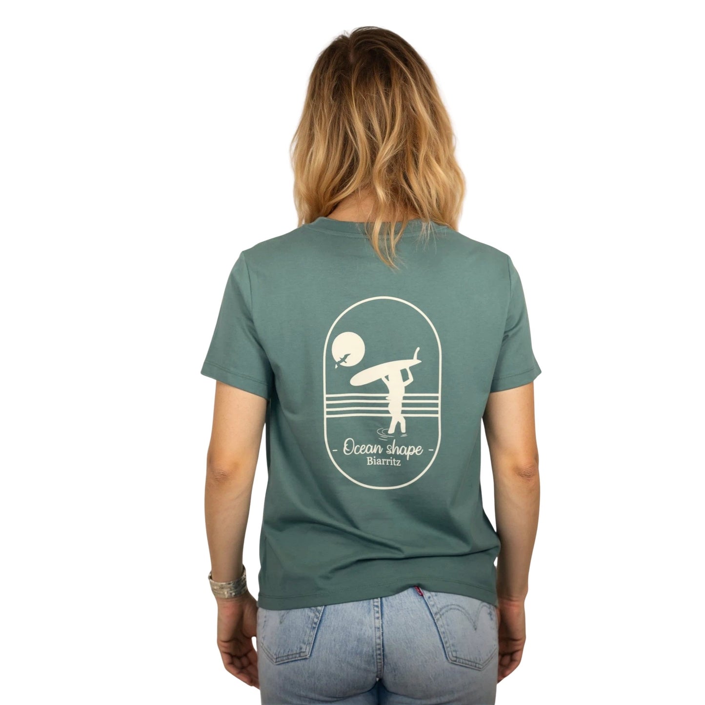 Tee-shirt femme en coton biologique vert sauge avec gros dessin surfeuse qui marche de dos et écriture ocean shape Biarritz écru dans le dos , vu de dos sur mannequin femme 