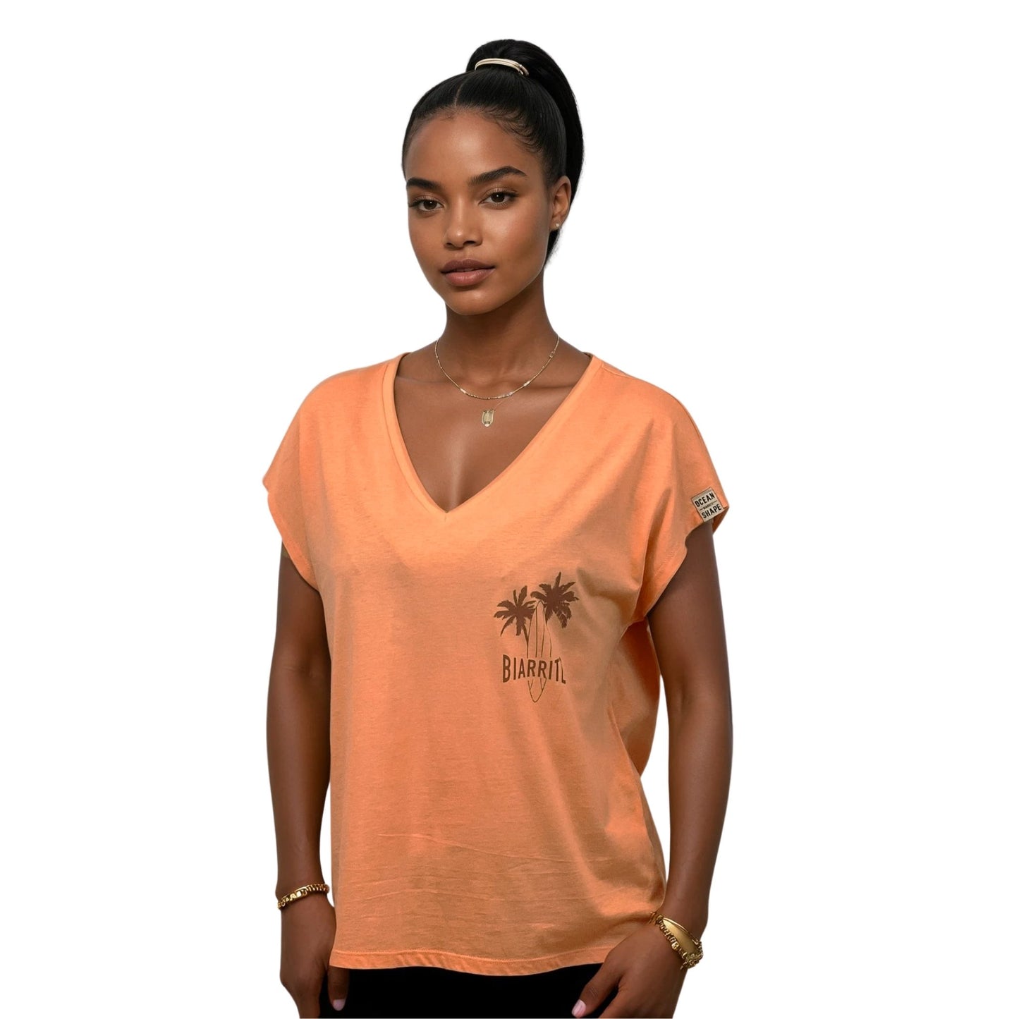 tee-shirt femme en coton biologique couleur abricot, col en V. Vu de face sur mannequin femme.
Petit dessin marron clair de palmiers, planche de surf + écriture Biarritz sur la poitrine gauche.